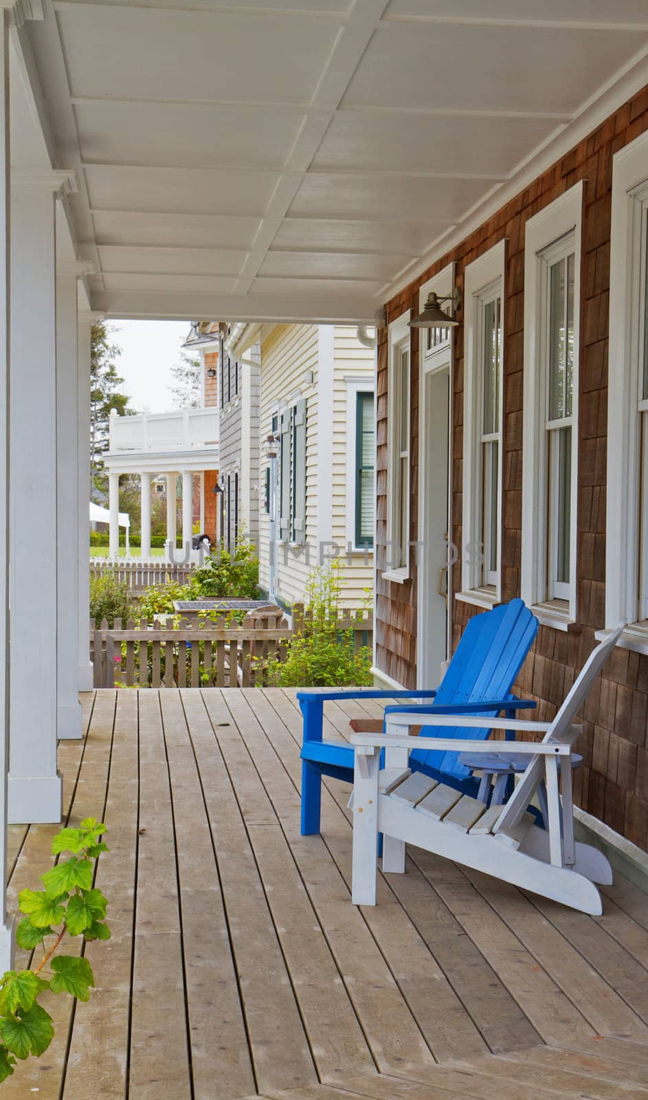 Blue and white adirondack chairs on a the wood porch of a brown shake home