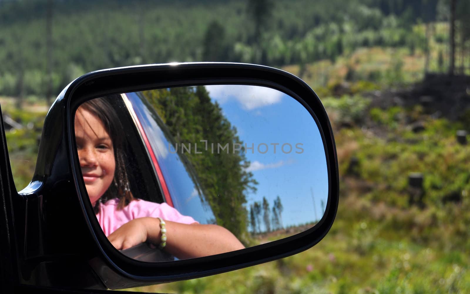 A young girl seen in a rear view mirror on a trip in rural environment.
