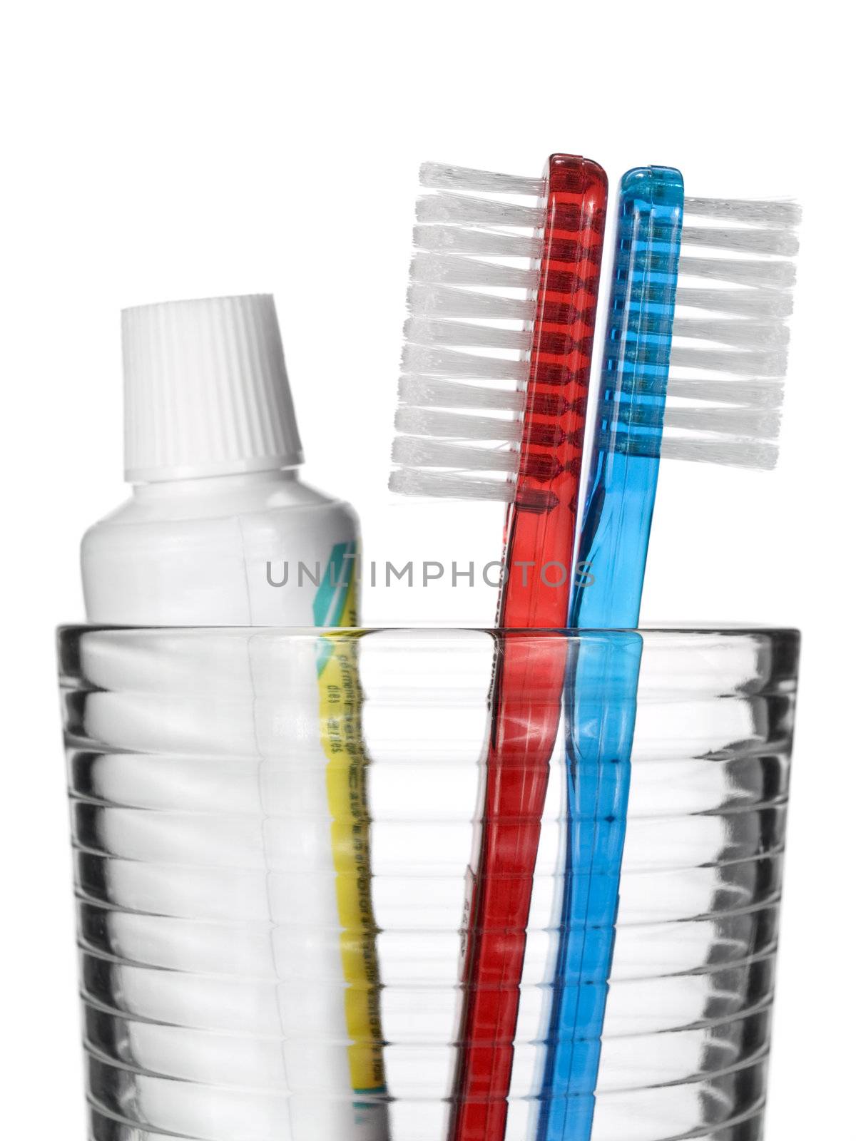 Two toothbrushes and a tube of toothpaste in a glass over white background.