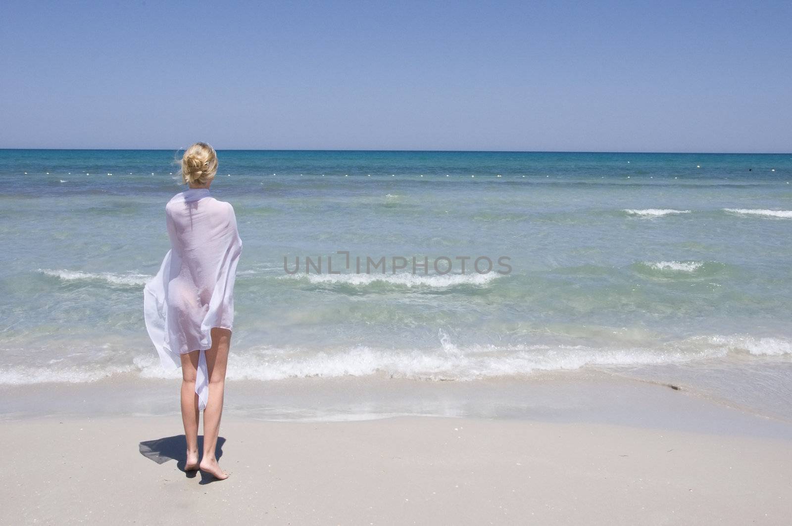 beautiful young girl in white walking on the beach by the blue sea