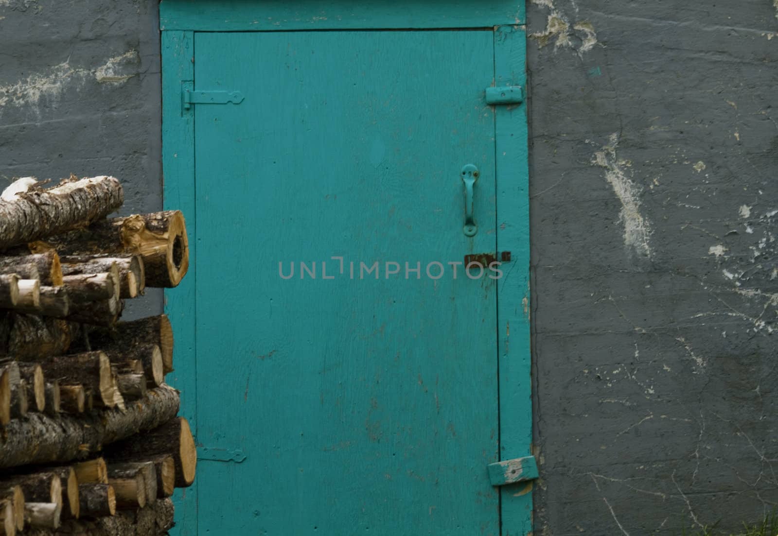 Rural frugality reflected in the turquoise door to an old root cellar fronted by stacked logs of winter firewood