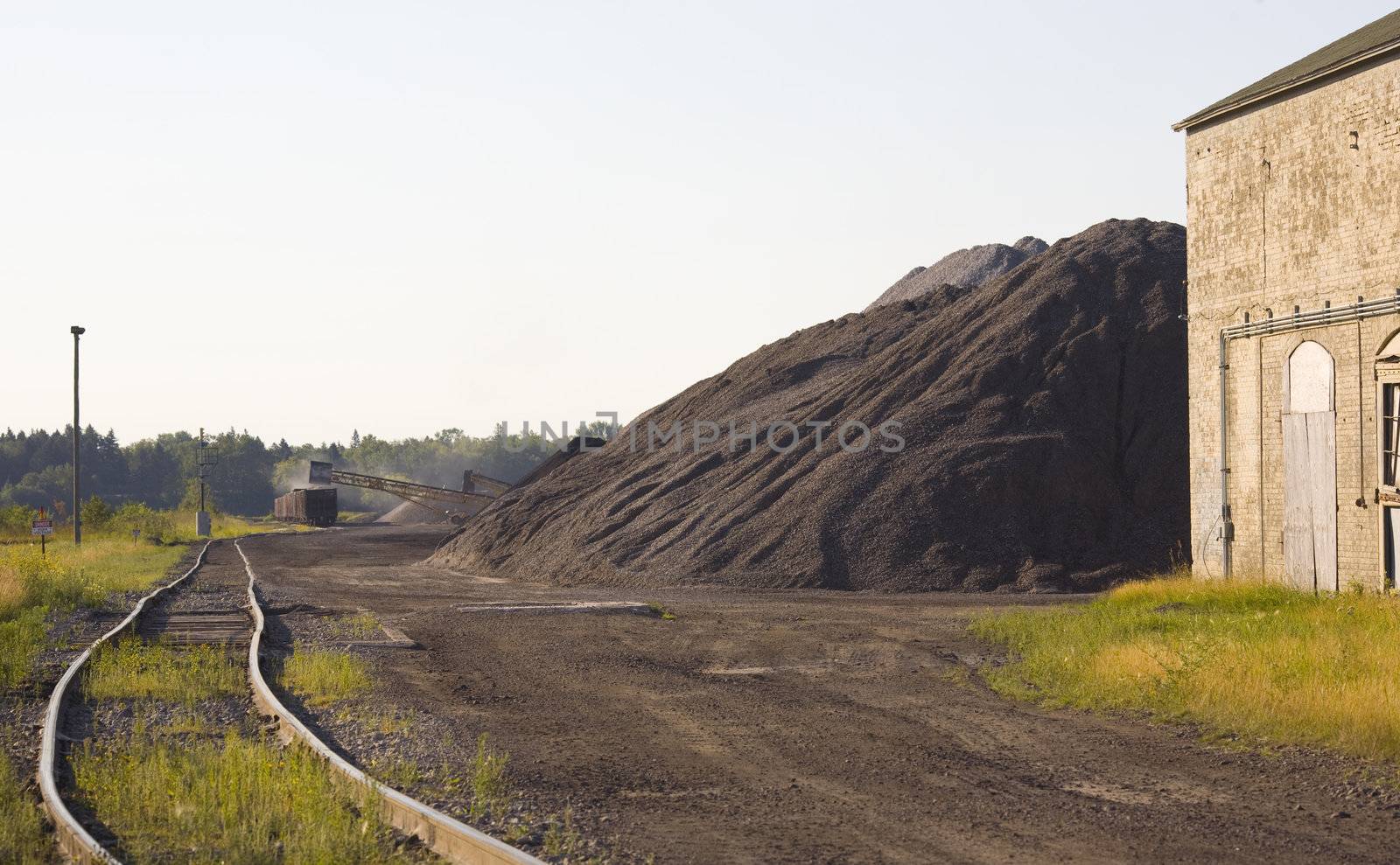 Coal loading in a rail yard on an old train next to massive stacks of coal.