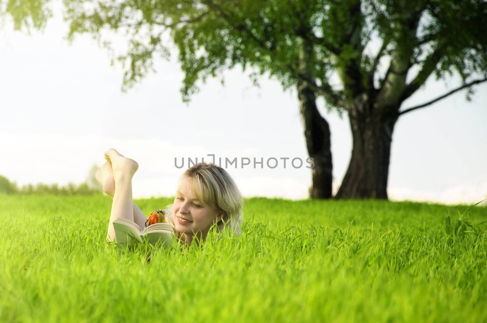 Young beautiful woman lays on green field and reads book