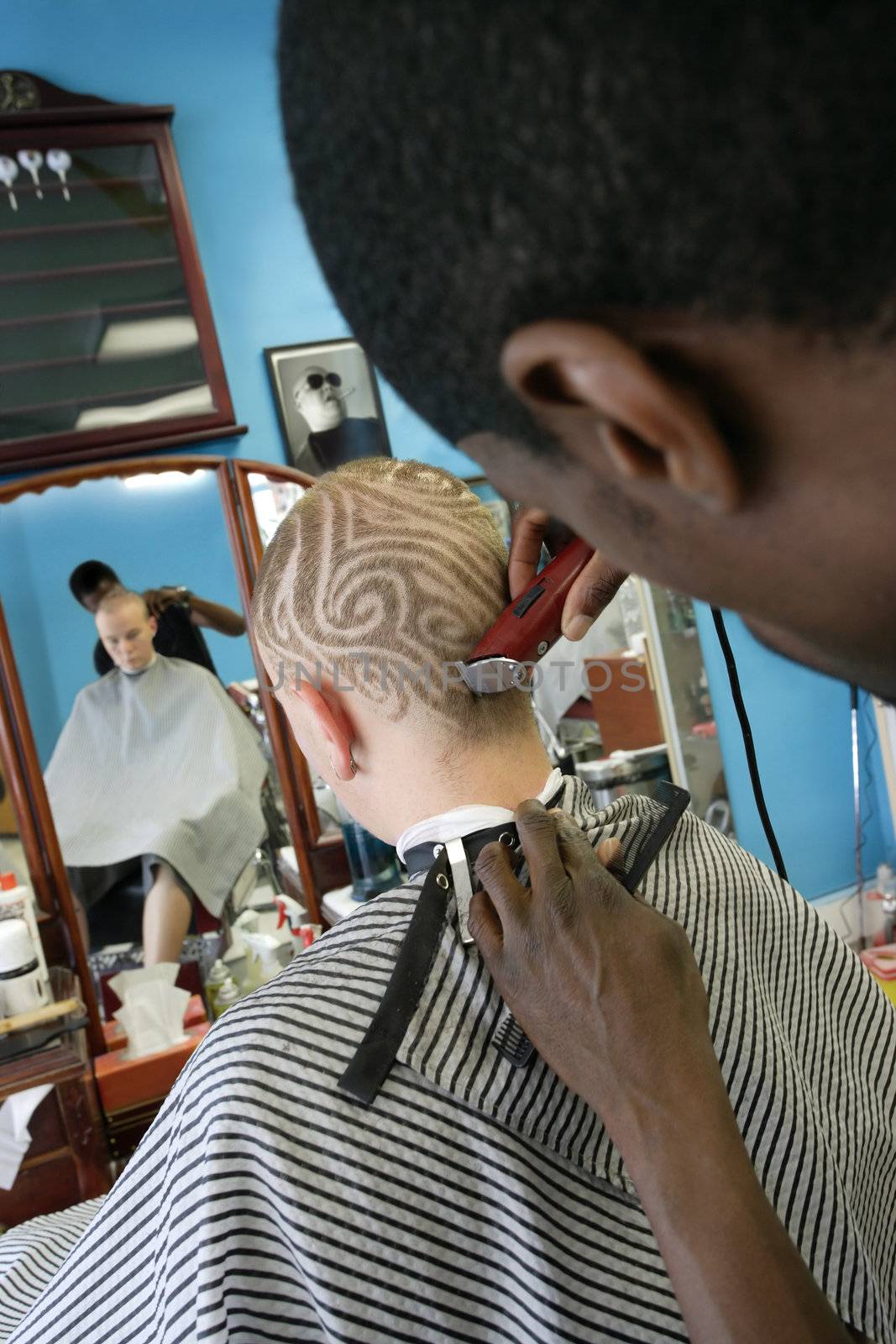 A barber cutting a pattern into a blond man's short hair. Three model releases attached. Third model release is for the photo in the frame on the wall, which has been edited in from an image from my portfolio. Property is a barbershop and tattoo studio - signed property release attached.
