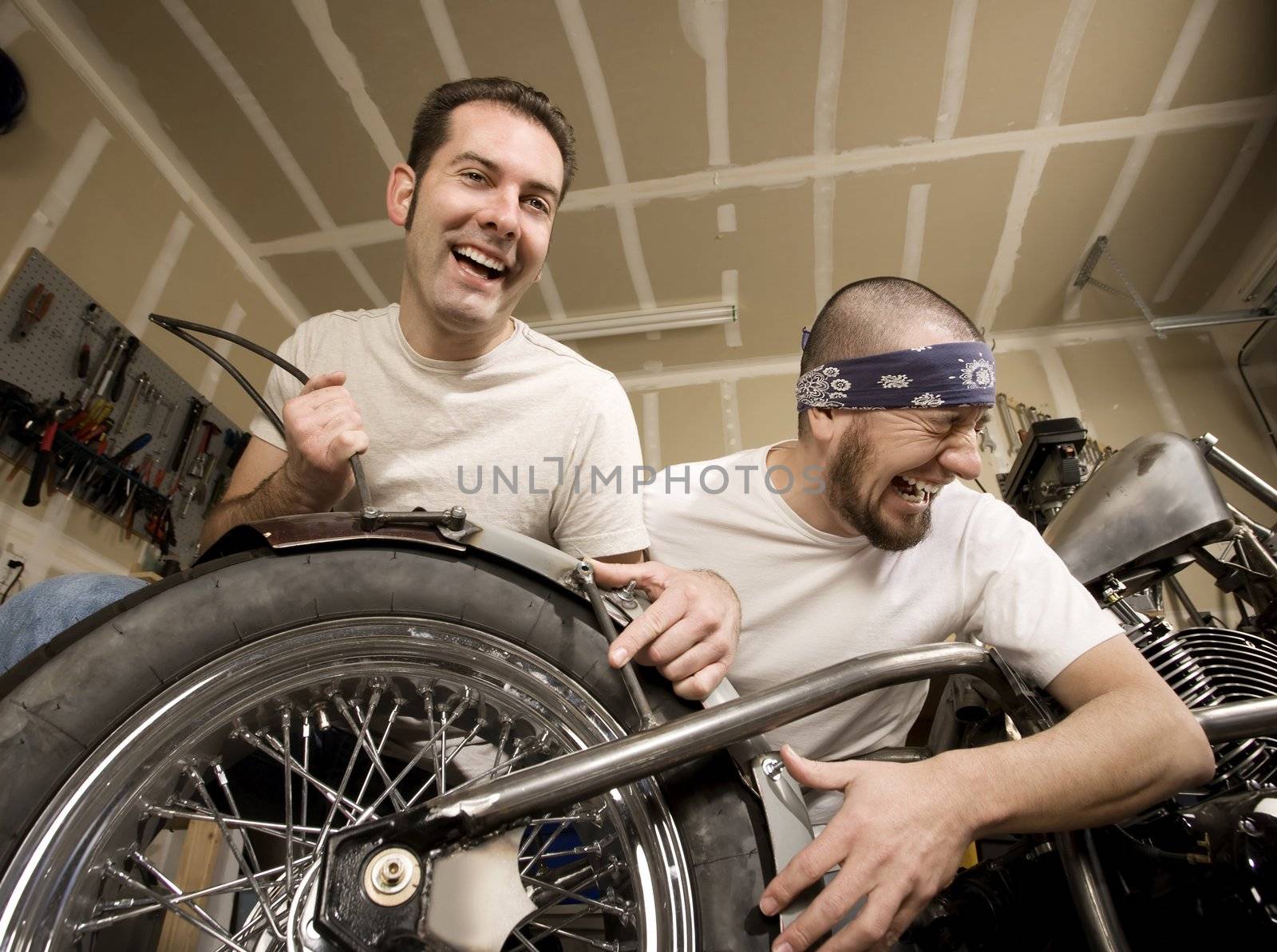 Two laughing men working on a chopper-style motorcycle