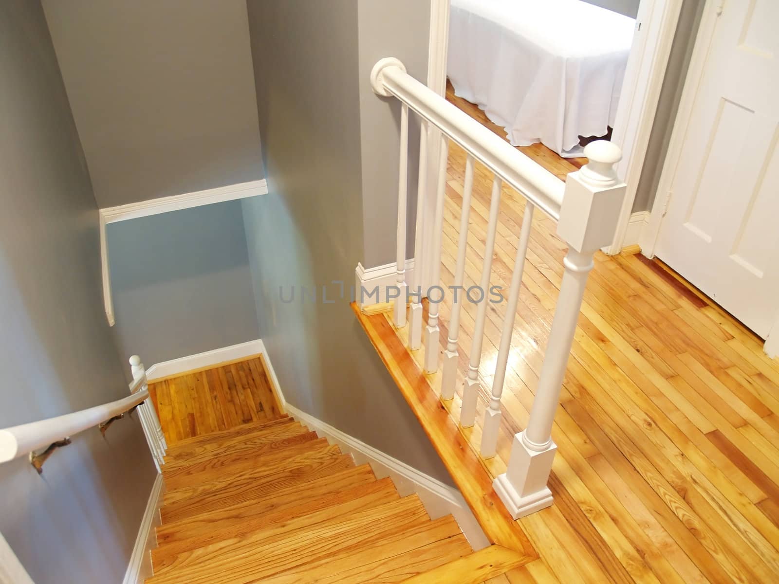 A refinished wooden floor and steps in a stairway. White painted railings and woodwork accent the classic gray walls