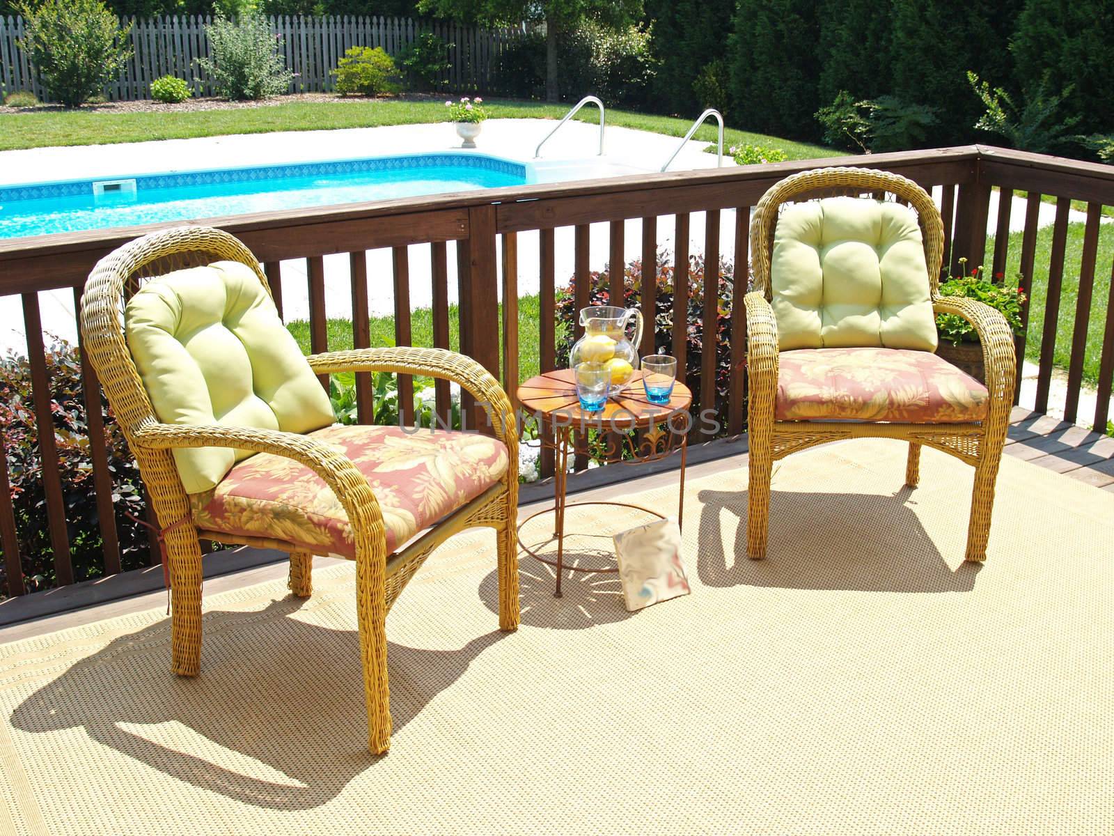 Two comfortable chairs on a patio overlooking a pool in the backyard