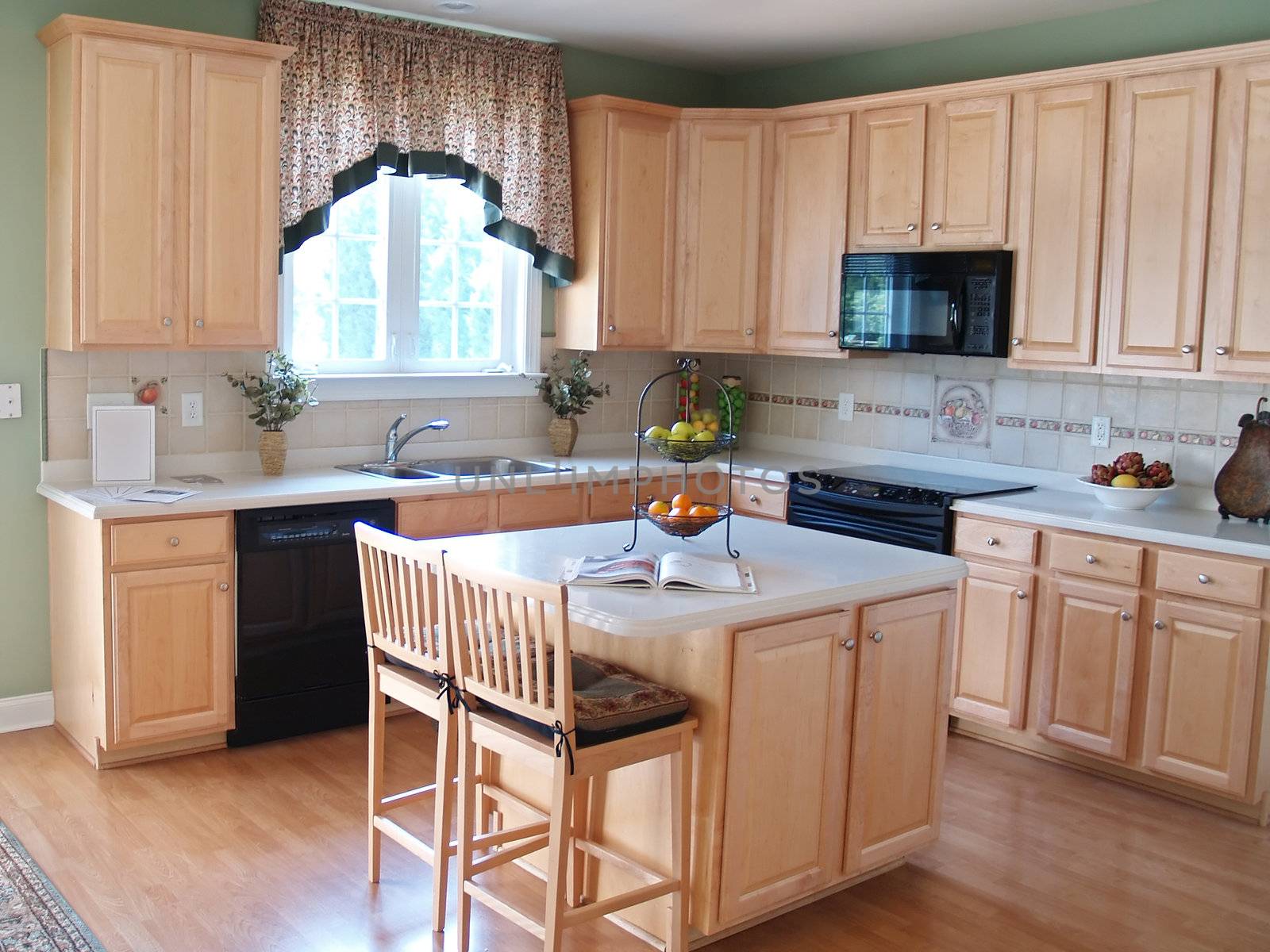 A modern kitchen with maple cabinets and hardwood floors. An island countertop with two barstool chairs make a perfect place for breakfast