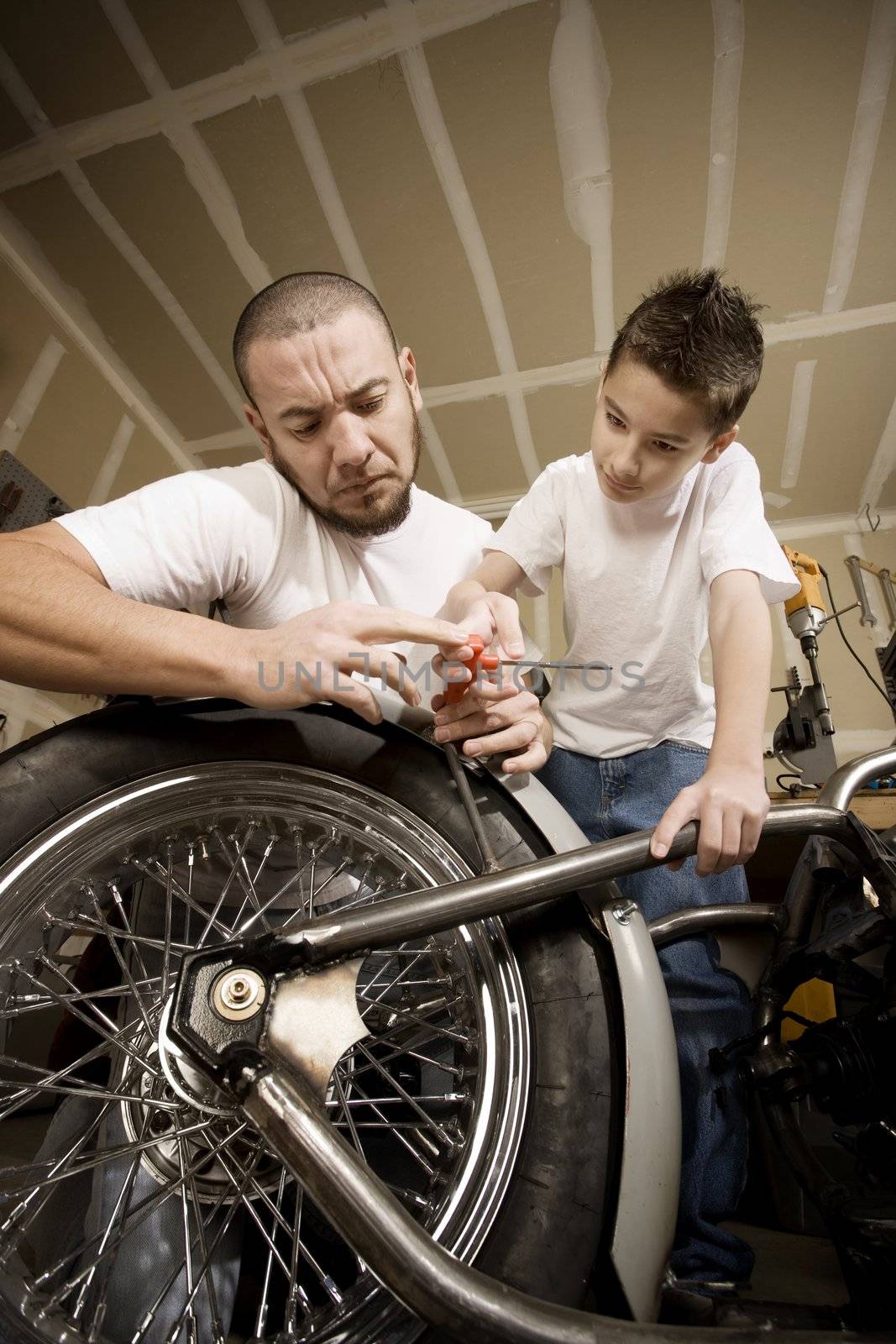 Hispanic father and son working on motorcycle in garage