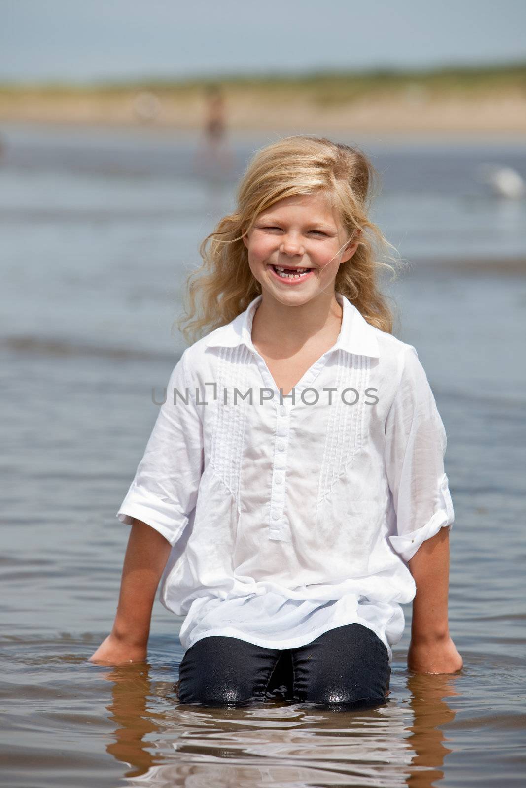Happy young girl sitting in the water getting wet