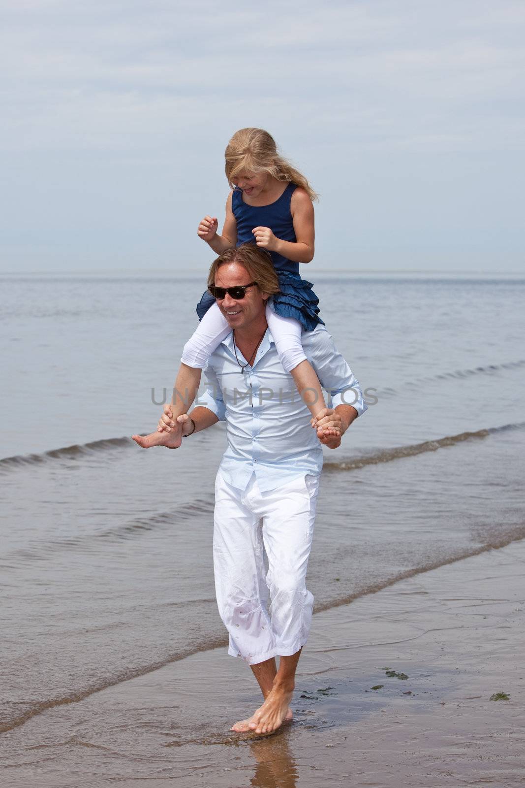 Cute young girl sitting on dad's shoulders playing in the surf