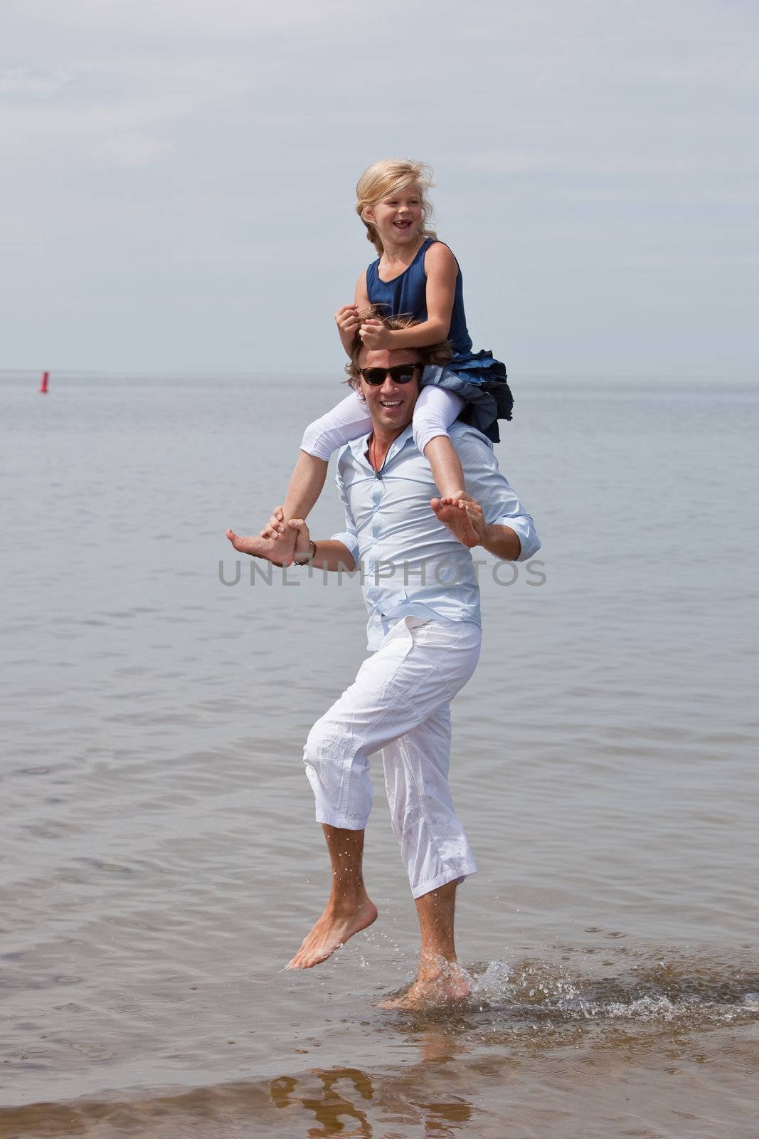 Young girl sitting on dad's shoulders who is running around in the water