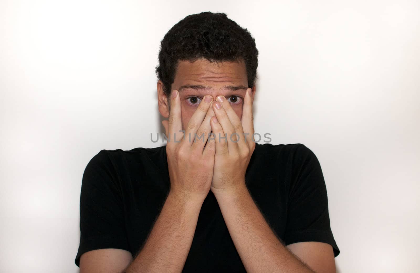 Young man covering his face in fear on isolated background