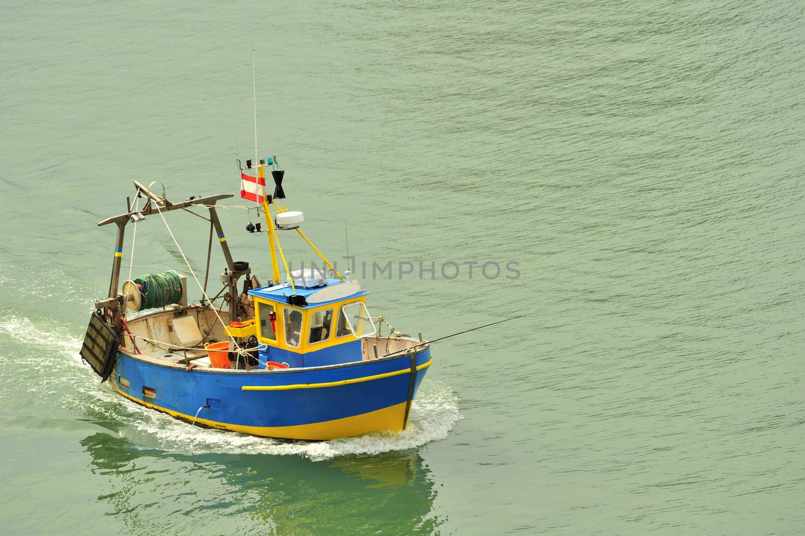 A small fishing boat coming into harbour. Space for text on the water.