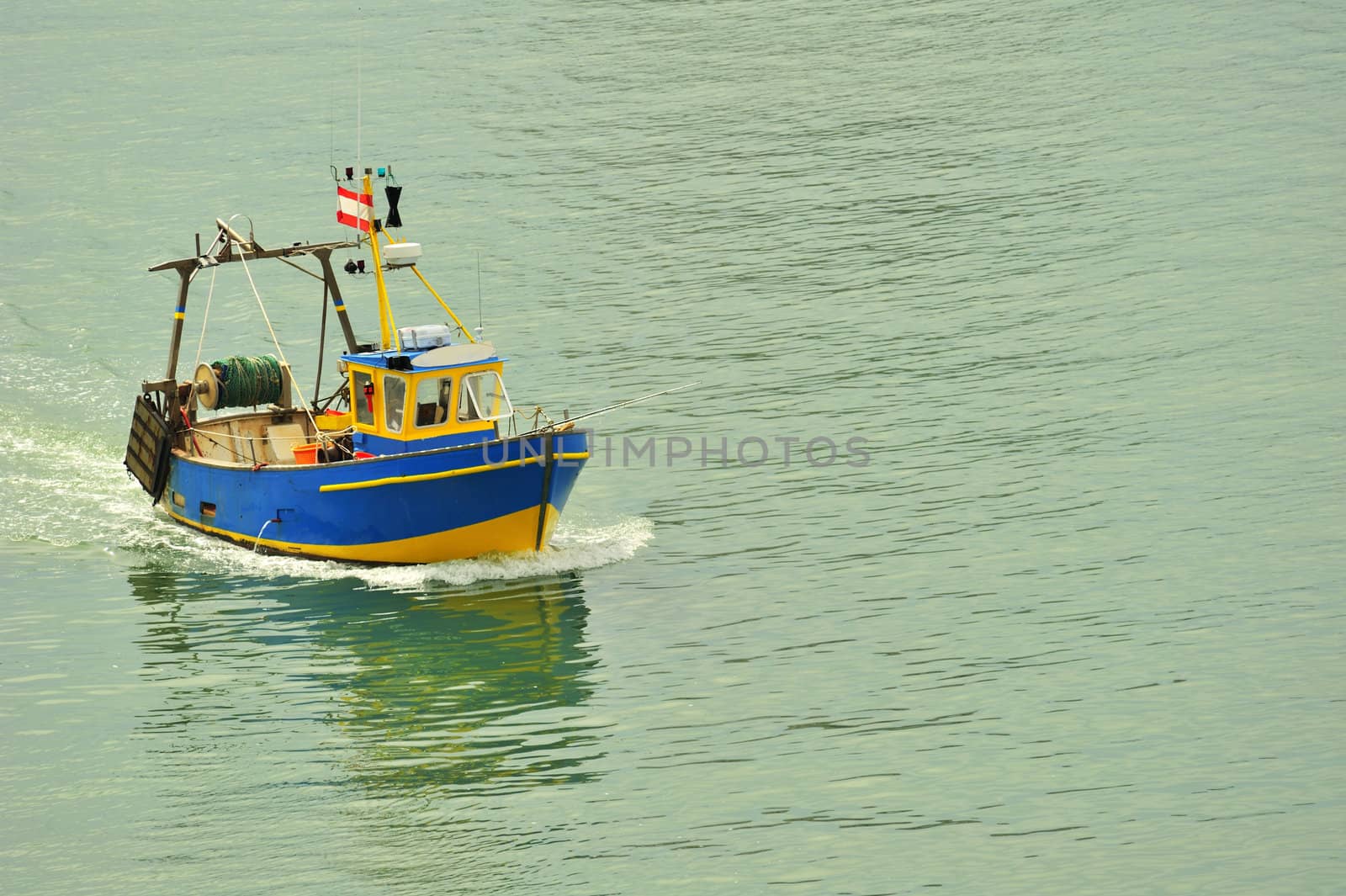 A small fishing boat coming into harbour. Space for text on the water.