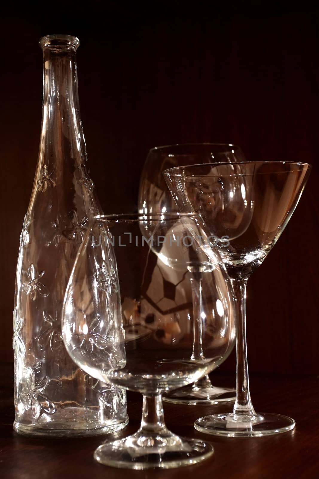 Still-life from crystal glasses and glass bottles against a dark background