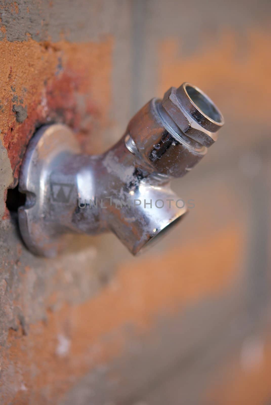 A chrome commercial grade hose bib or spygot on rough brick wall