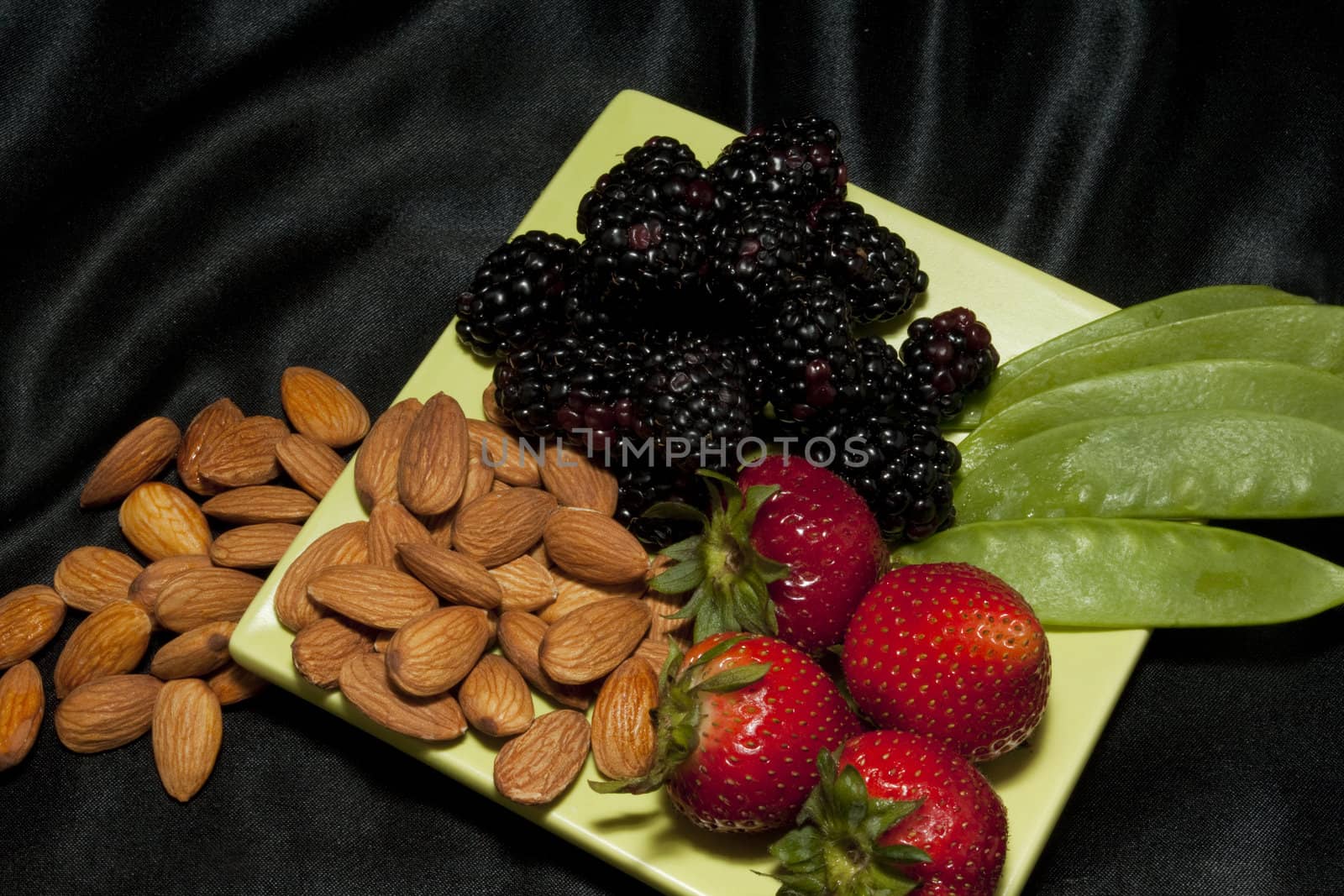 Berries, nuts, and snow pea pods on a light green plate against a black background are a healthy snack designed to refresh and keep fit