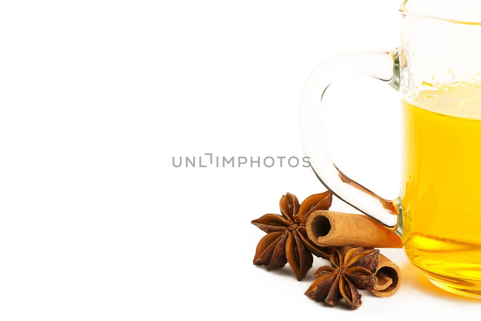 half glass with yellow tea, two cinnamon sticks and two star anise on white background