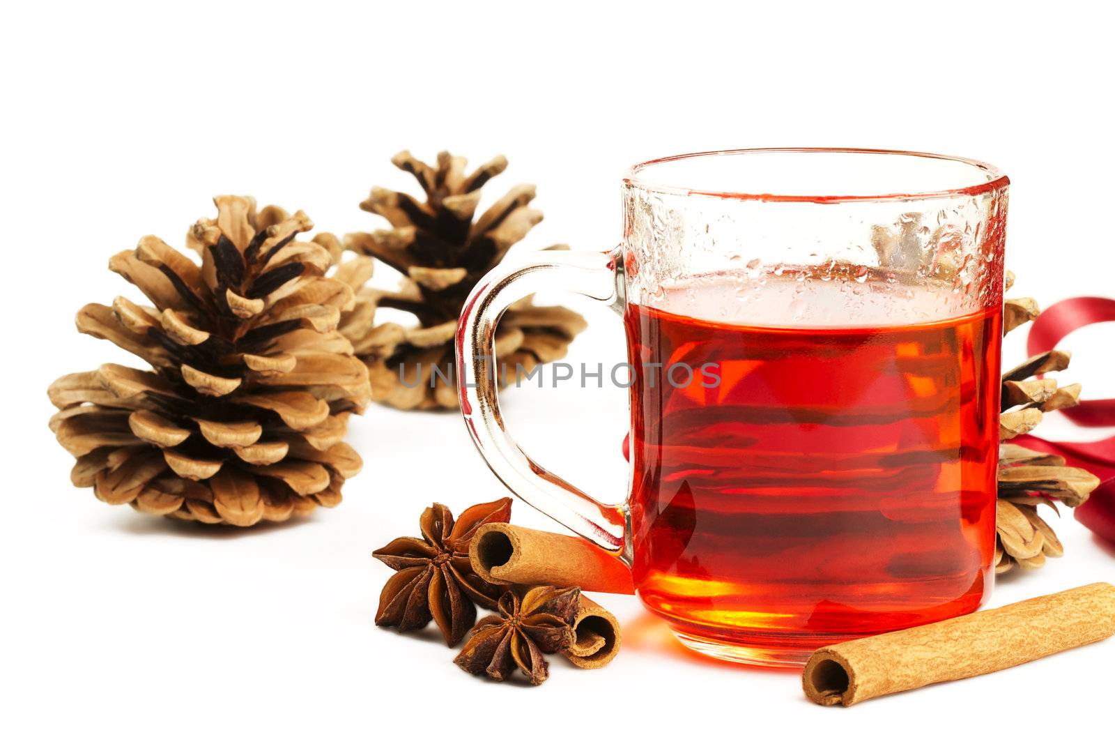 red tea in a glass, cinnamon sticks, star anise and some conifer cones on white background
