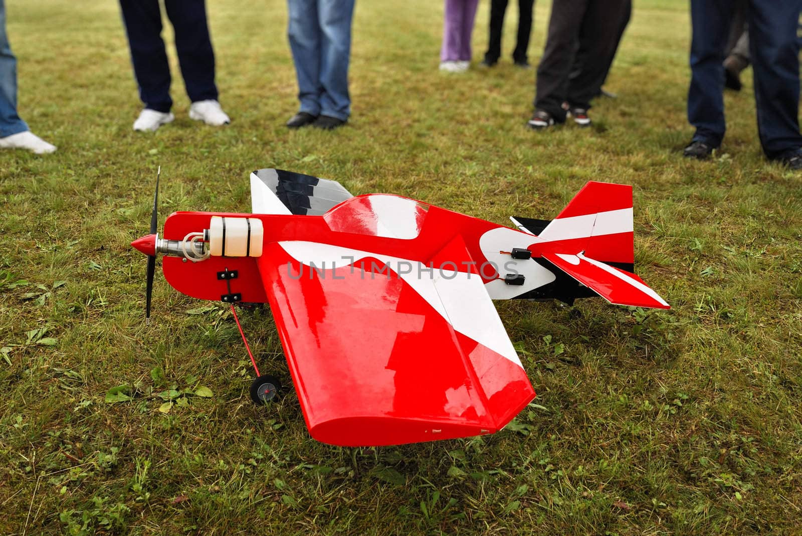Red and white radio controlled aircraft with methanol engine on a grassy field.