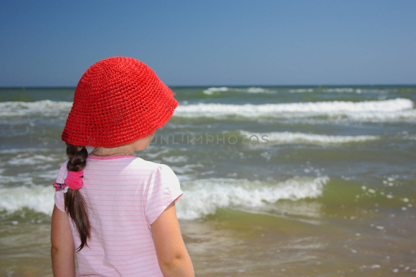 Girl in a red straw hat looking at the sea