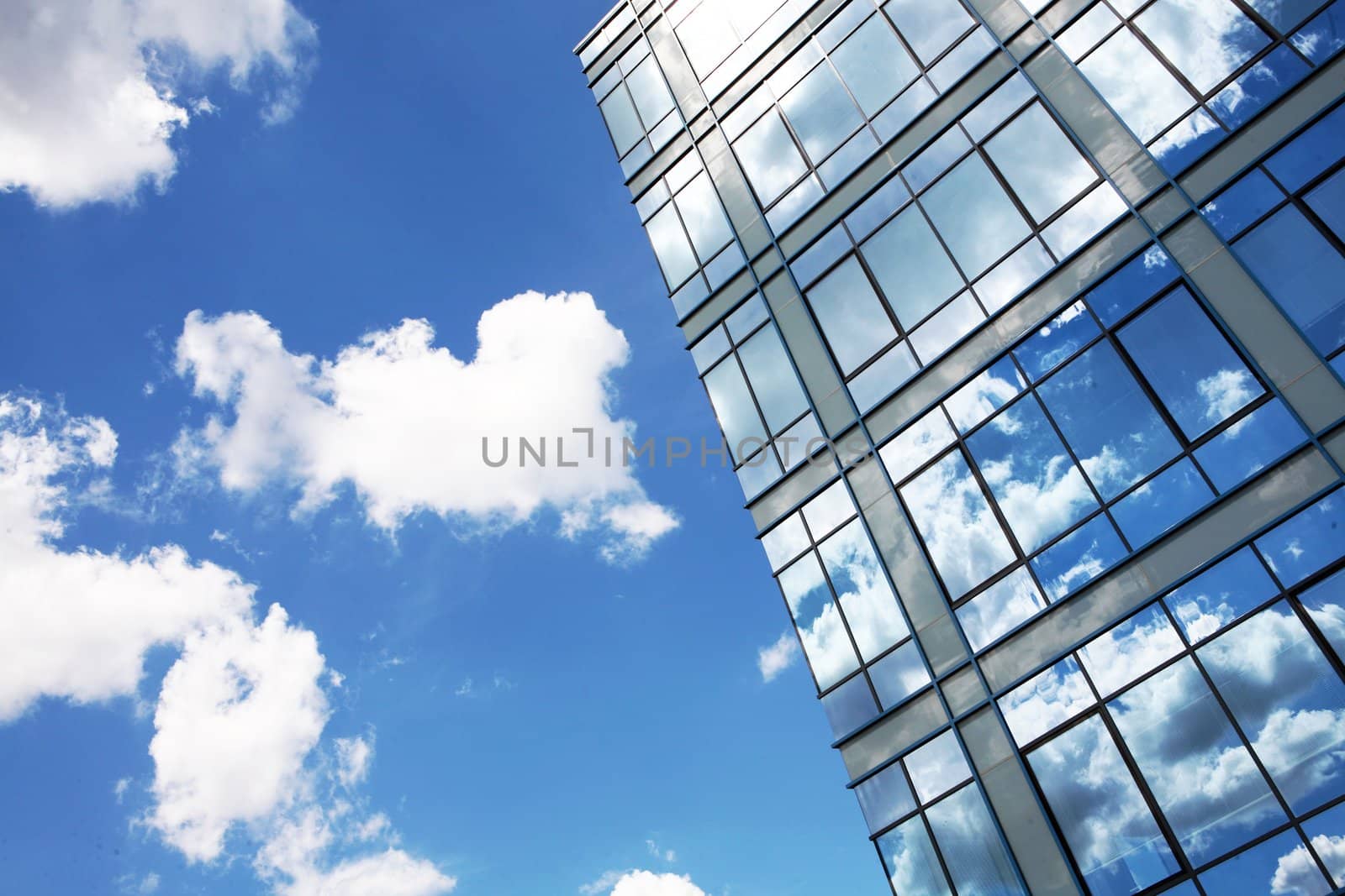 Modern glass building in perspective reflecting cloudy sky