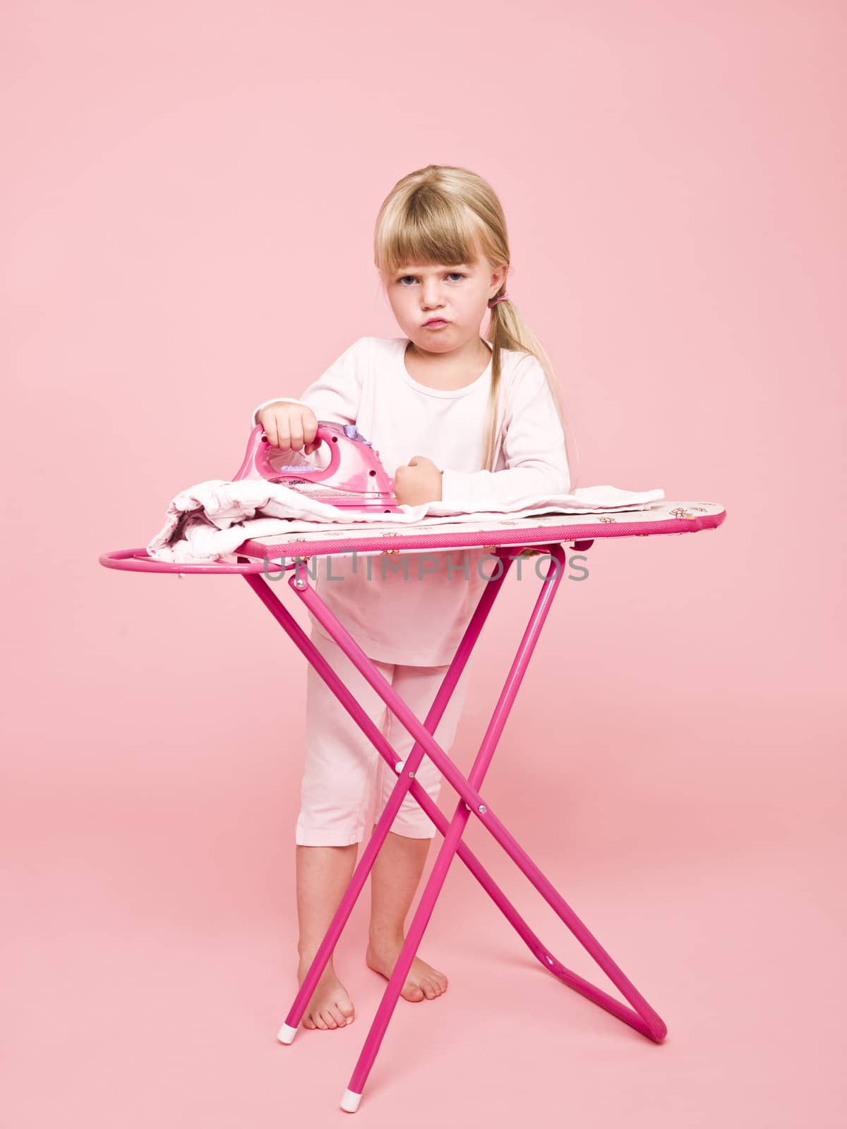 Angry girl ironing clothes towards pink background