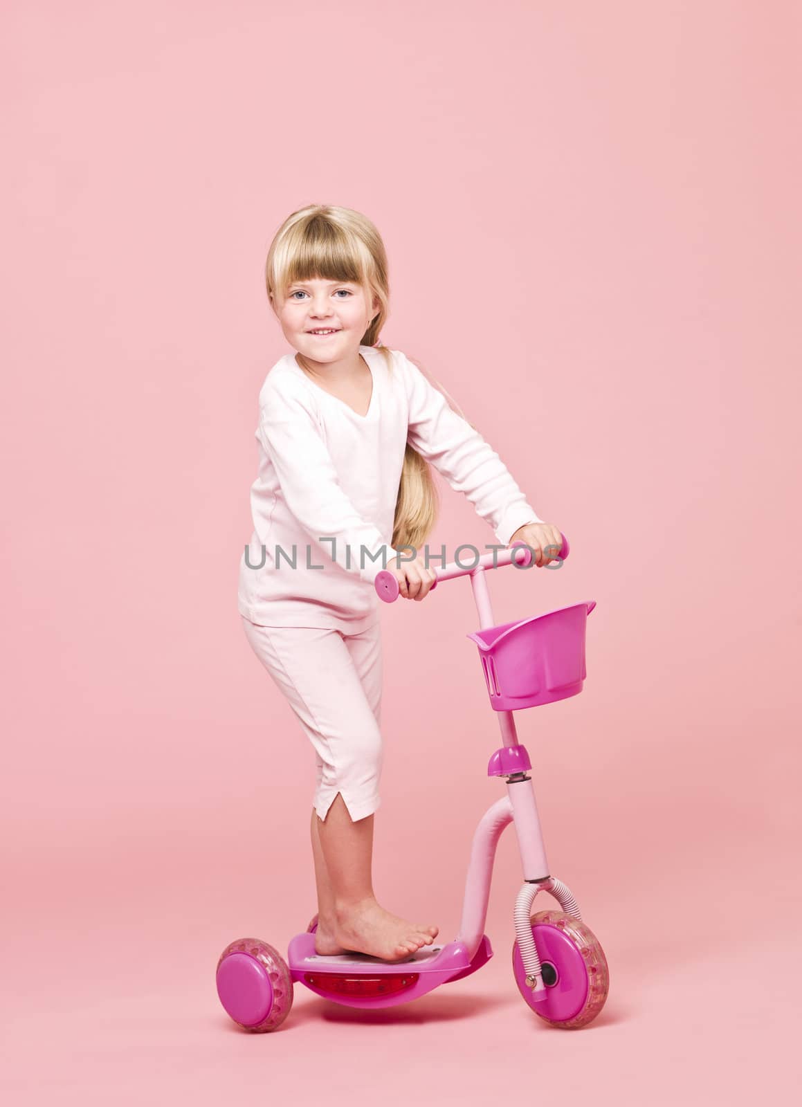 Young girl with a scooter towards pink background