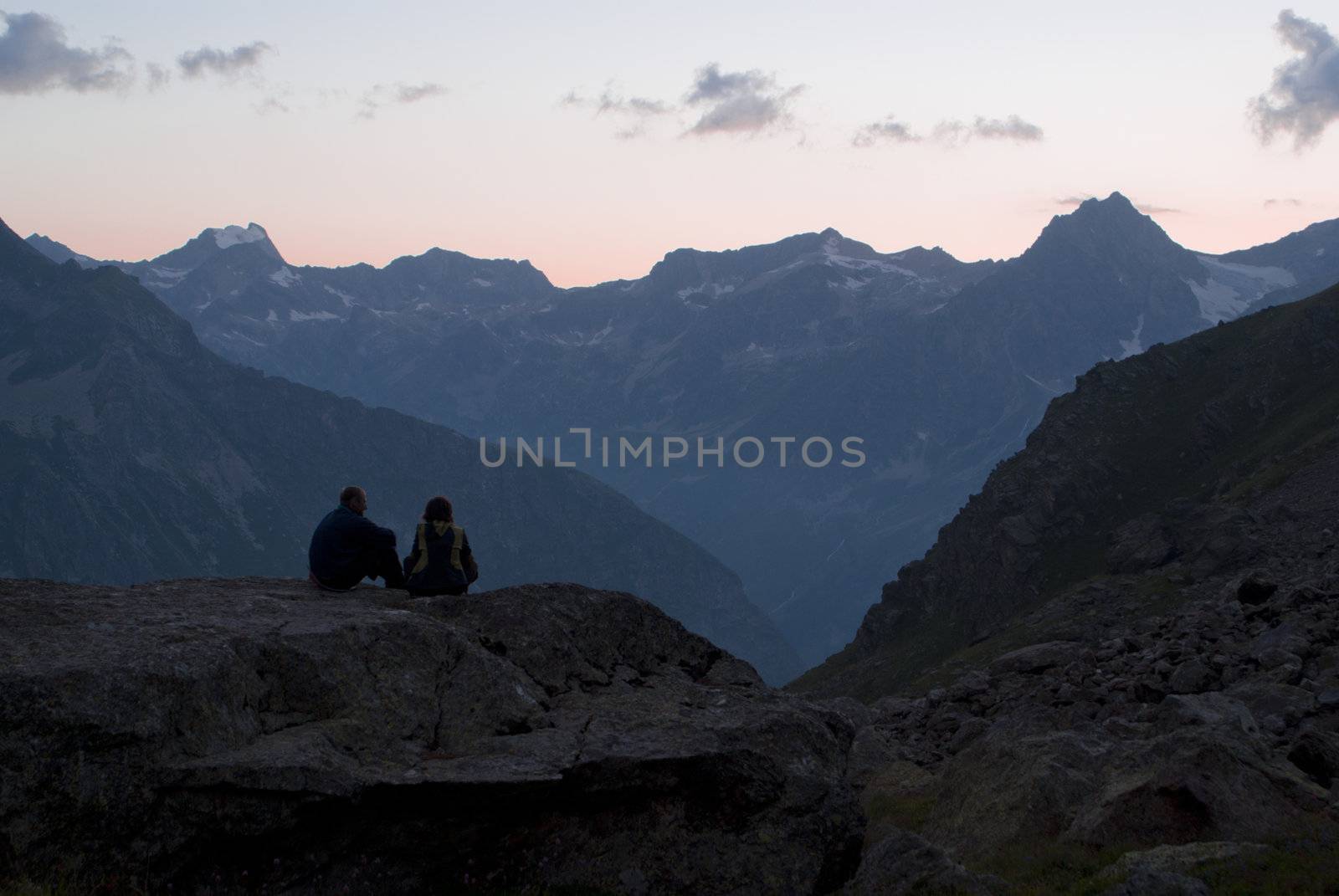 Man and girl sits on the stone in mountains
