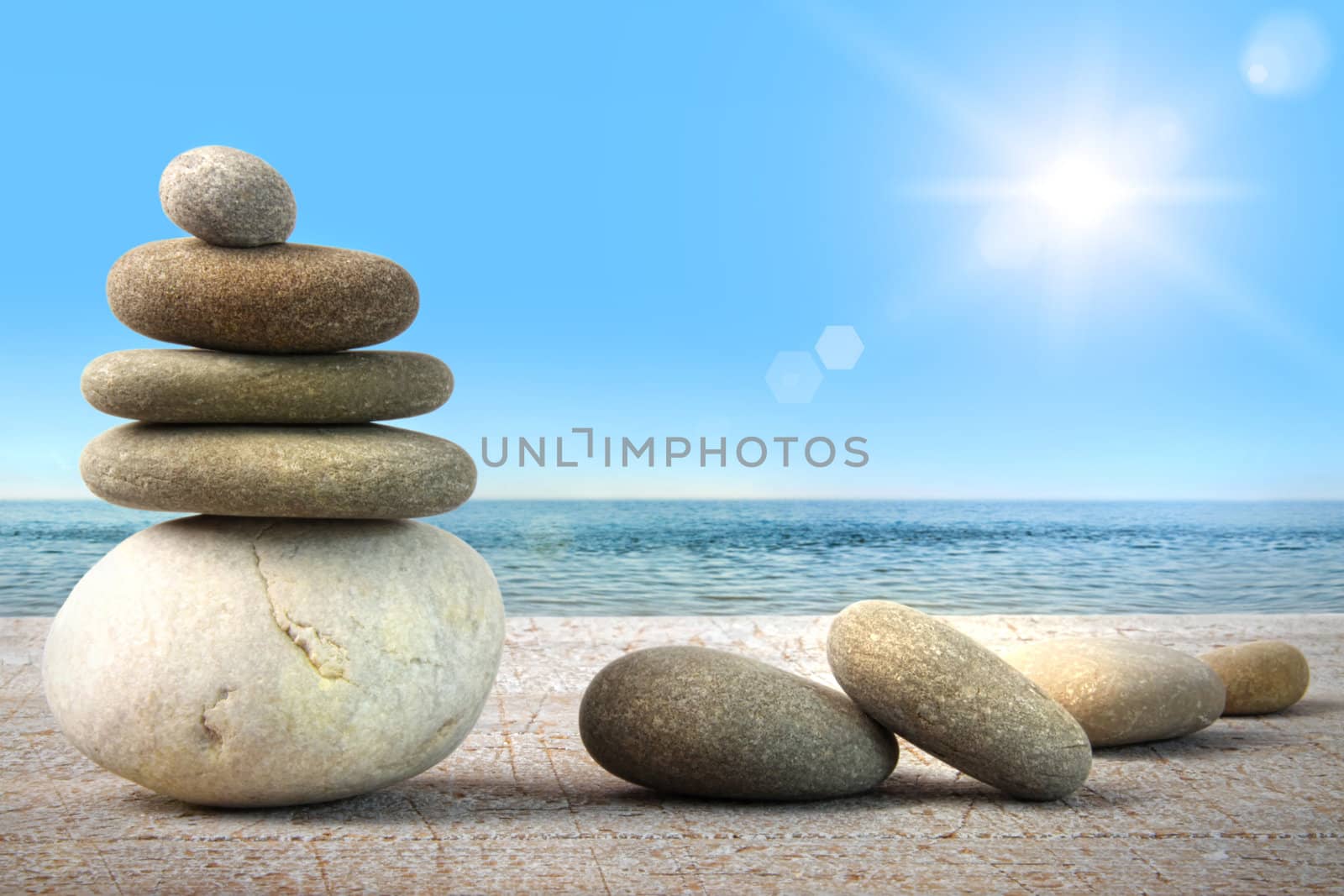Stack of spa rocks on wood against water and blue sky