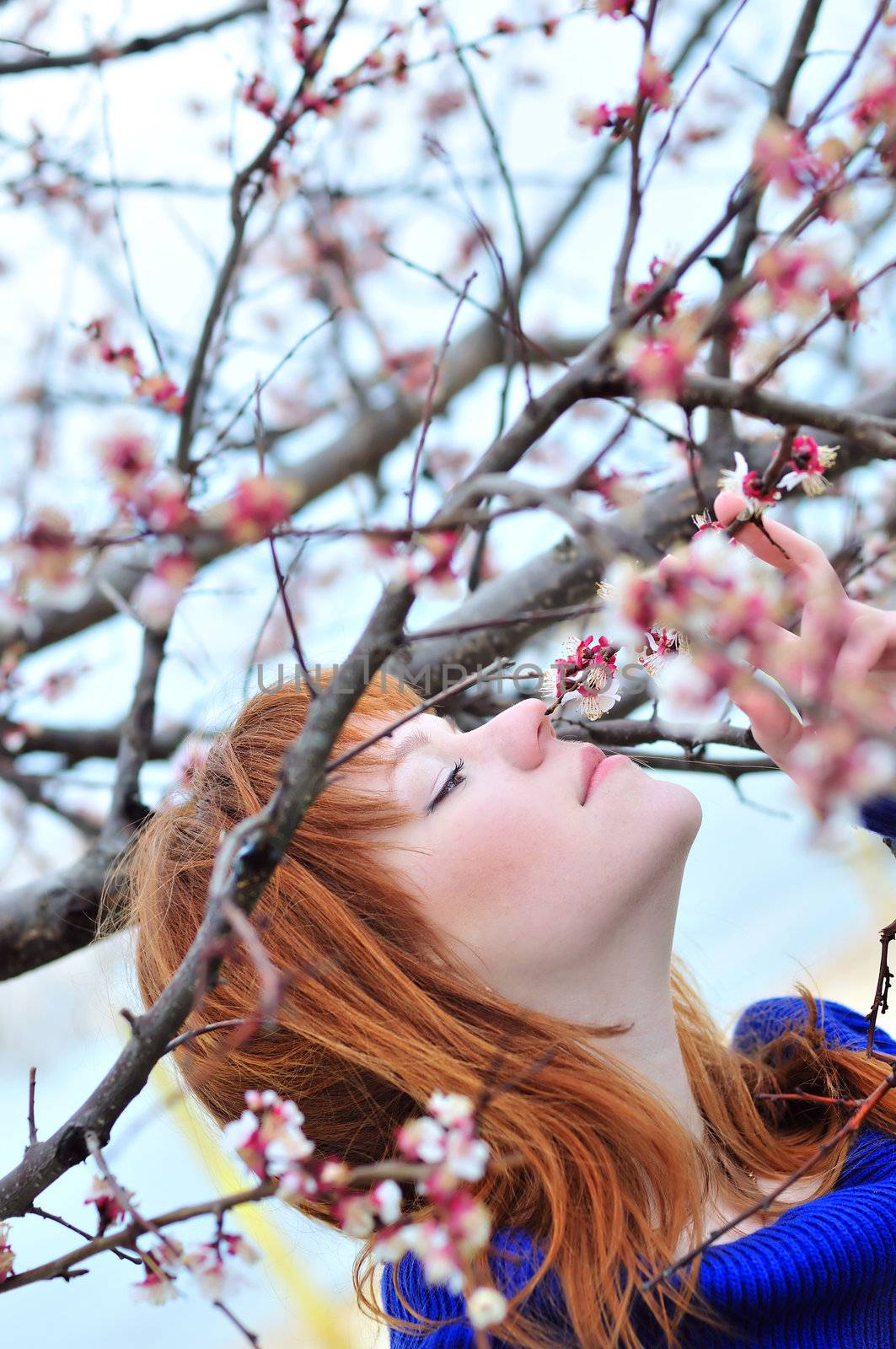 redheaded girl smelling blossom of peach tree