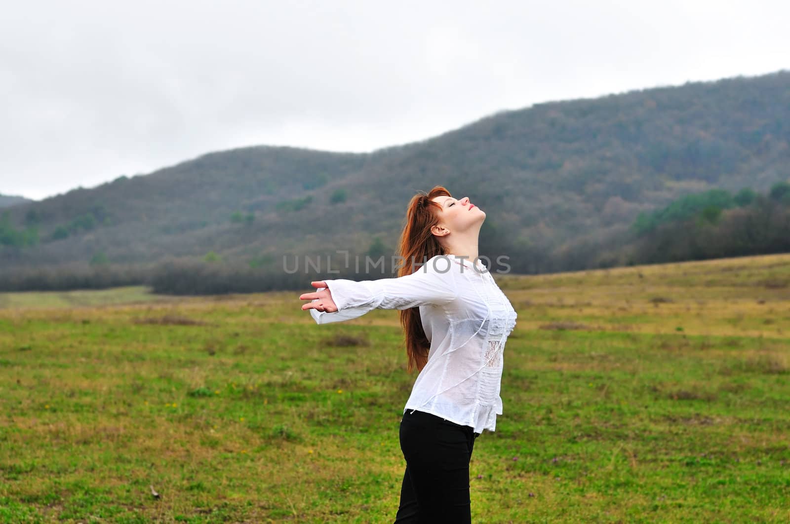 redheaded girl standing in fielad at one with nature, 	boughs reach out towards the sun