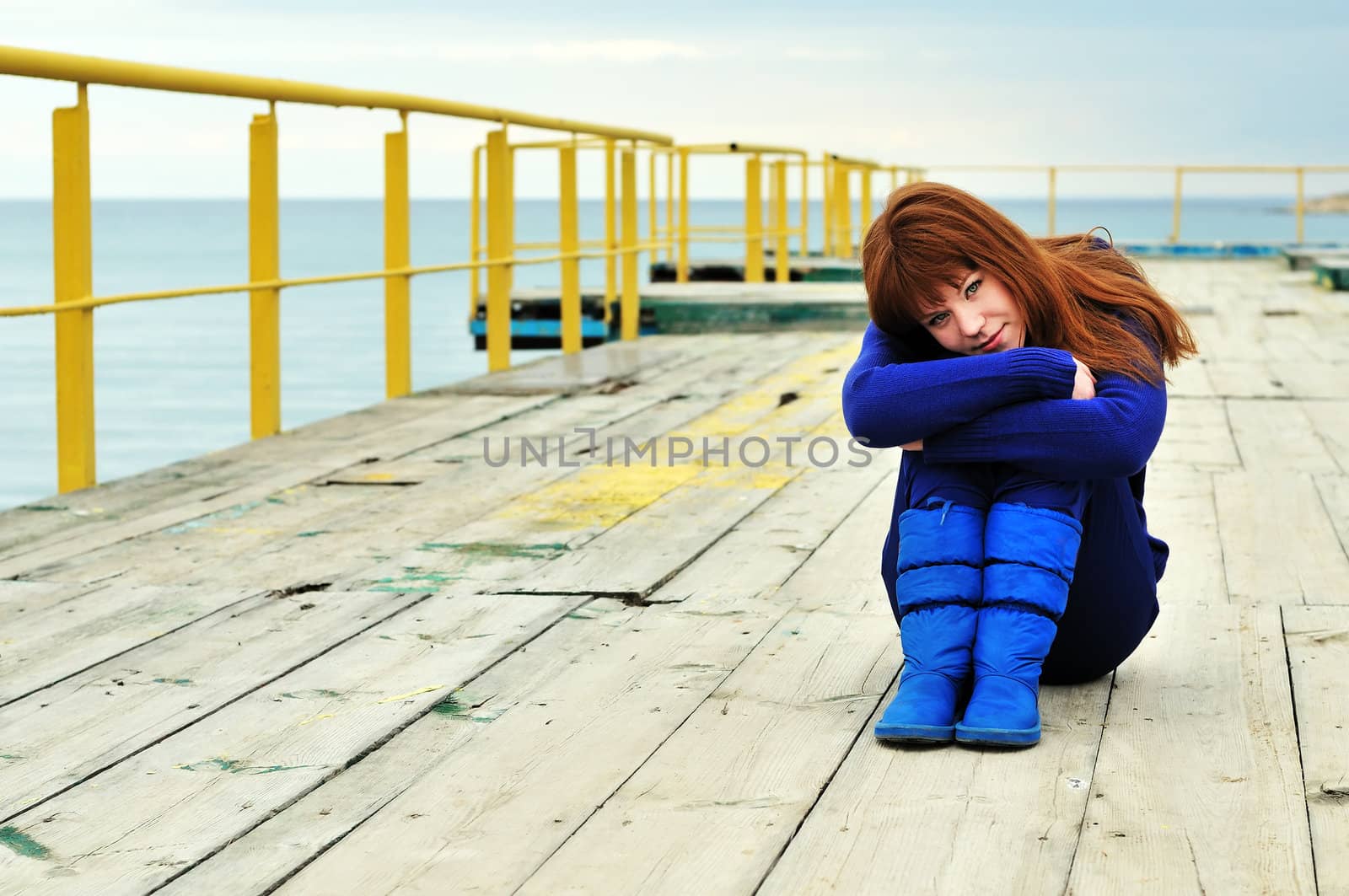 Young redheaded girl on a pier near the sea
