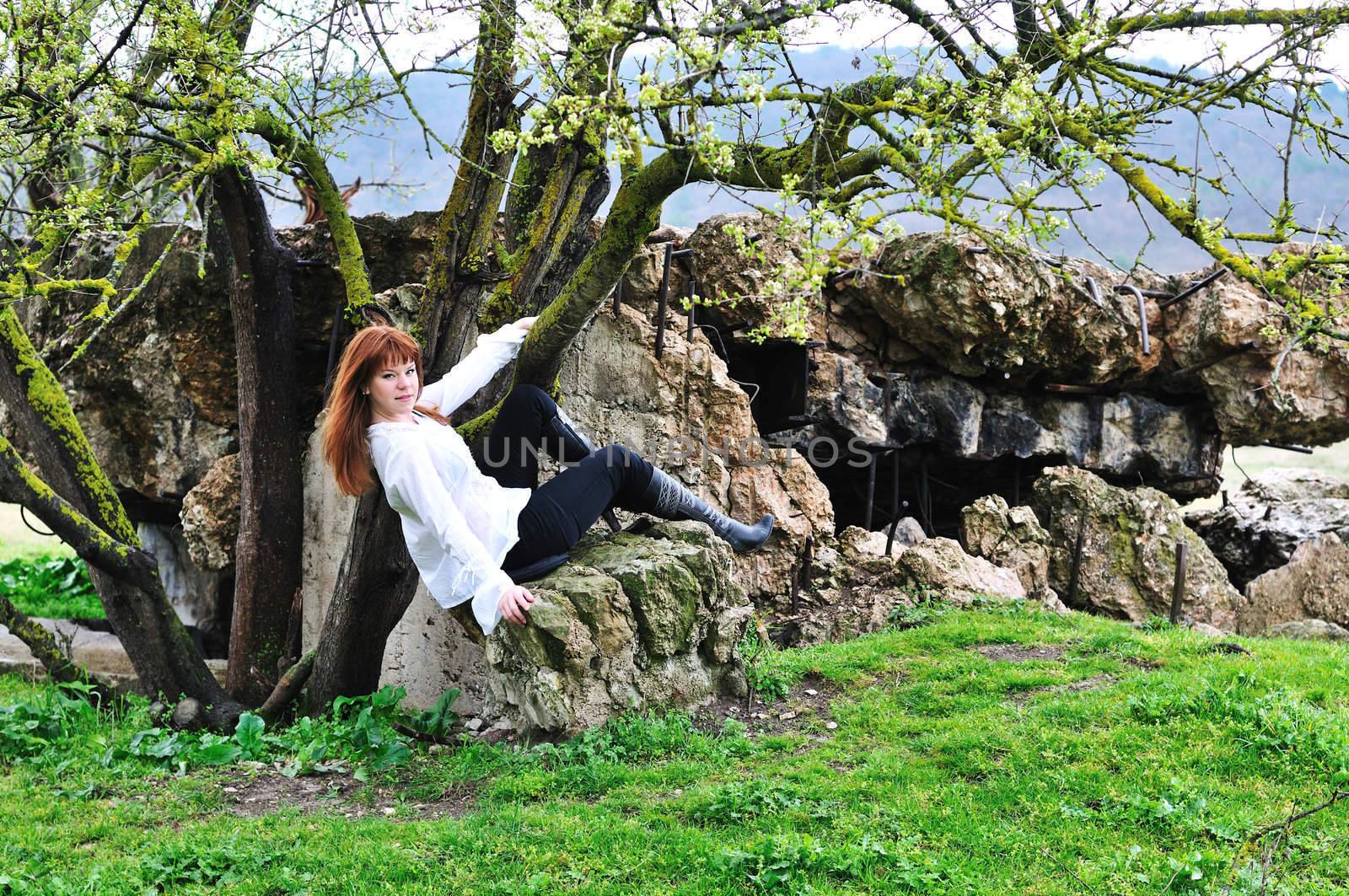 redheaded gorgeous girl sitting between tree and stone