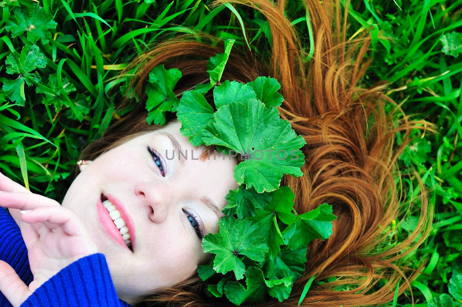 face of redheaded girl laying on the green grass with crown from leaves