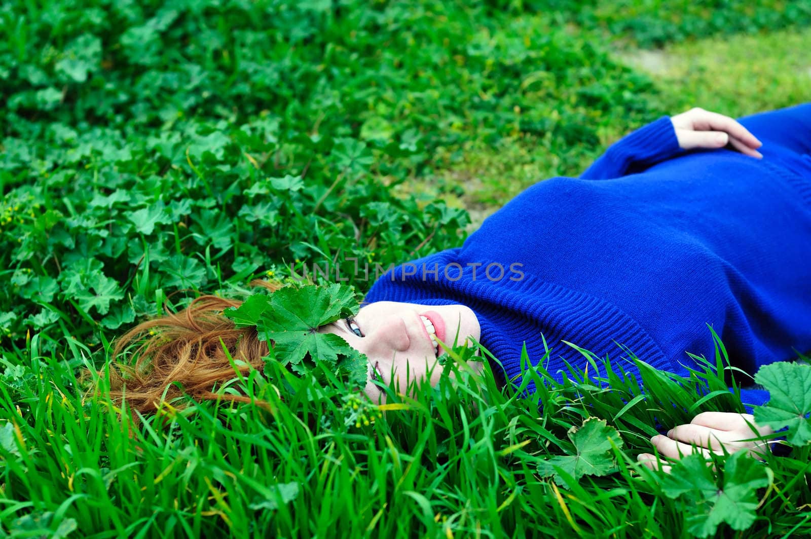  redheaded girl laying on the green grass with crown from leaves 