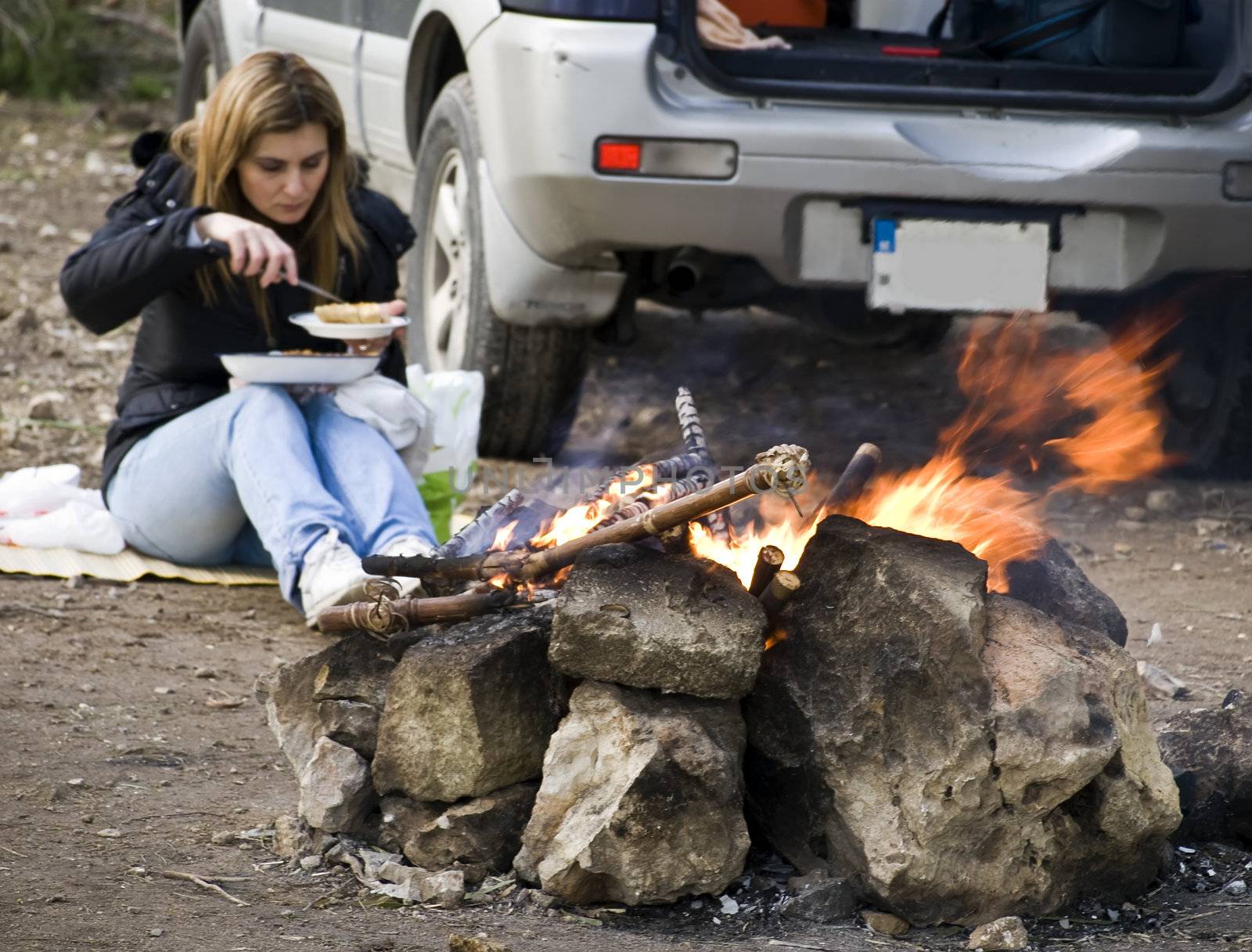A woman next to SUV and burning bonfire excellent to portray outdoor leisure activities such as camping