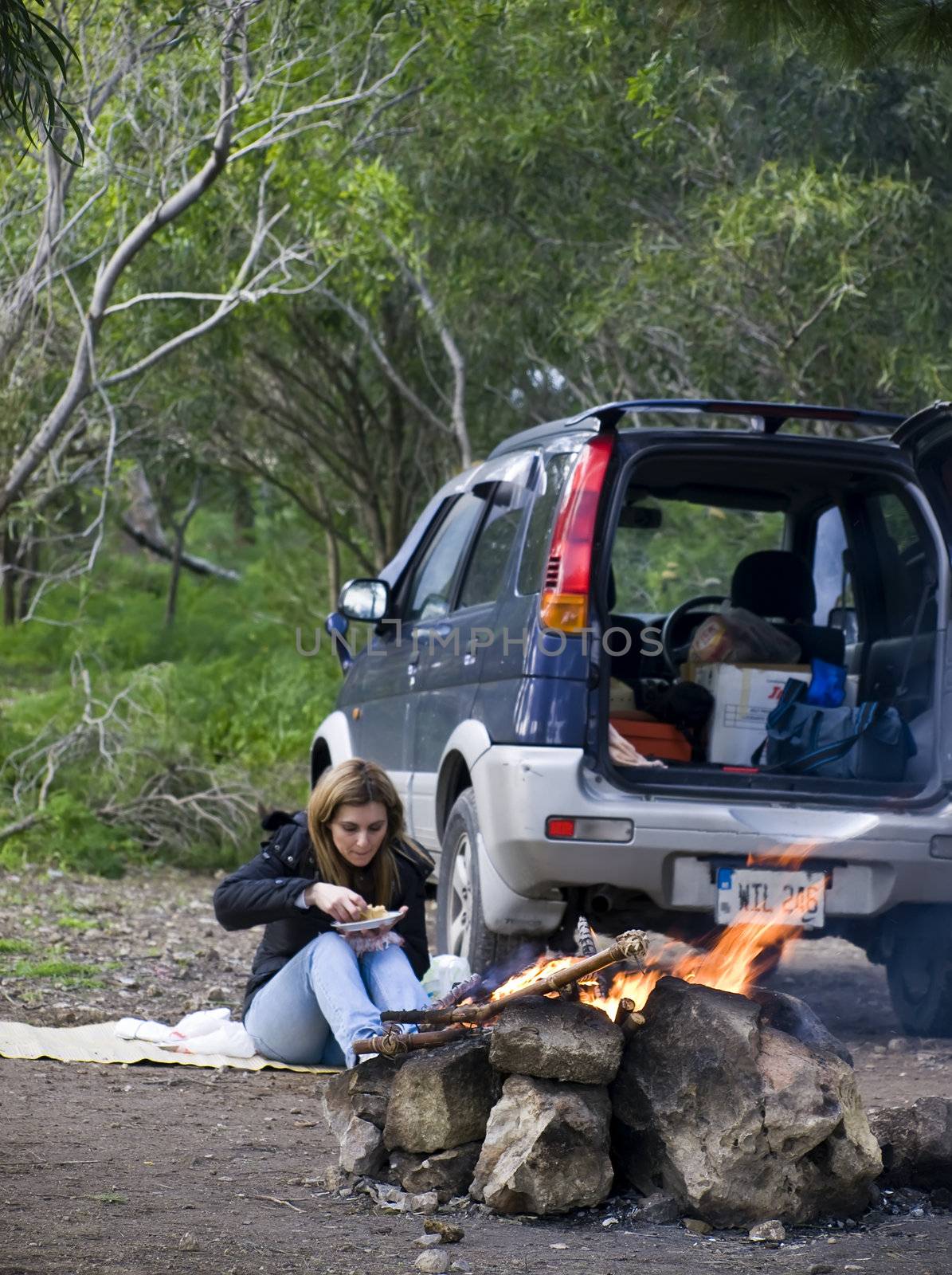 A woman and SUV next to burning bonfire excellent to portray outdoor leisure activities such as camping