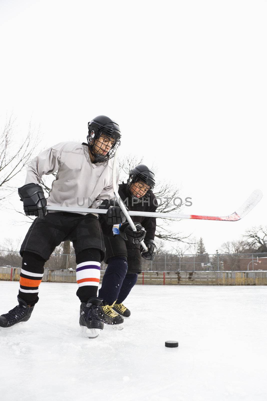 Two boys in ice hockey uniforms playing hockey on ice rink.