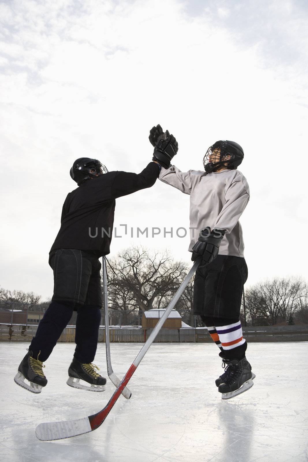 Two boys in ice hockey uniforms giving eachother high five on ice rink.