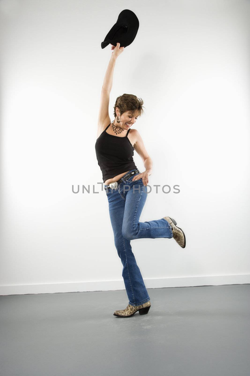Full length portrait of pretty Caucasian woman holding up cowboy hat in playful pose.