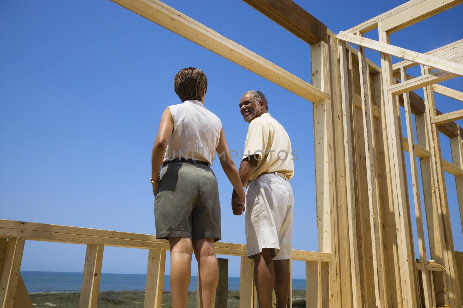 African American middle aged couple holding hands in new home construction at beach.