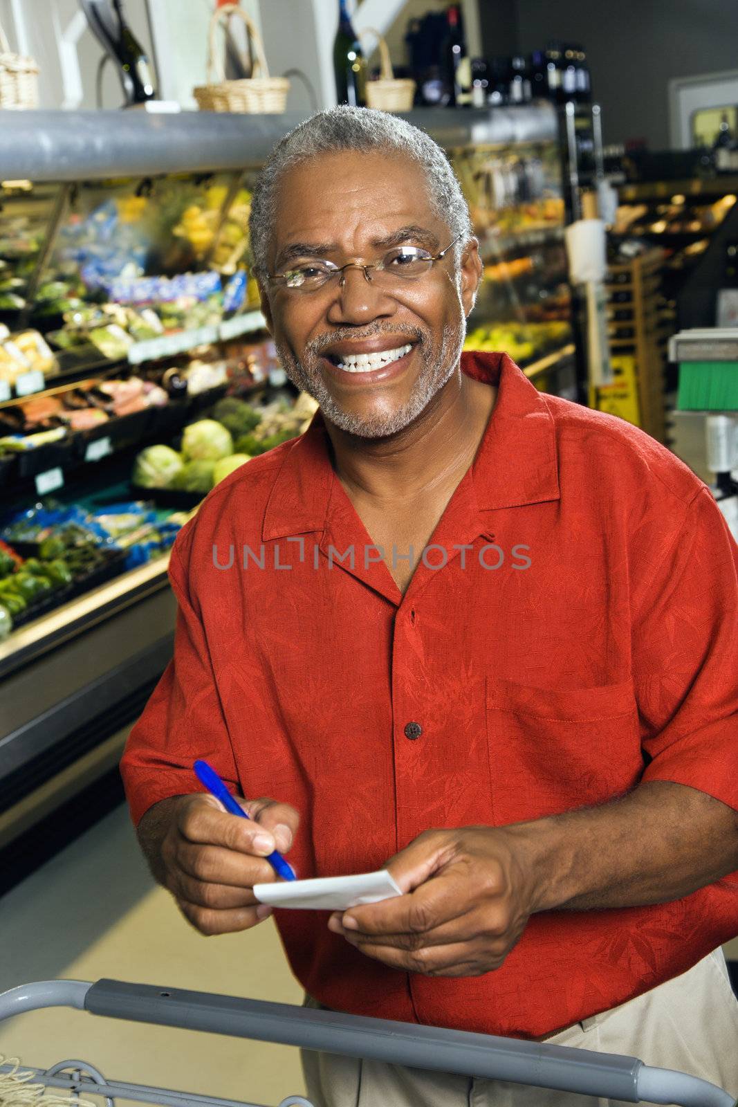 Middle aged African American man in grocery store holding shopping list and smiling at viewer.