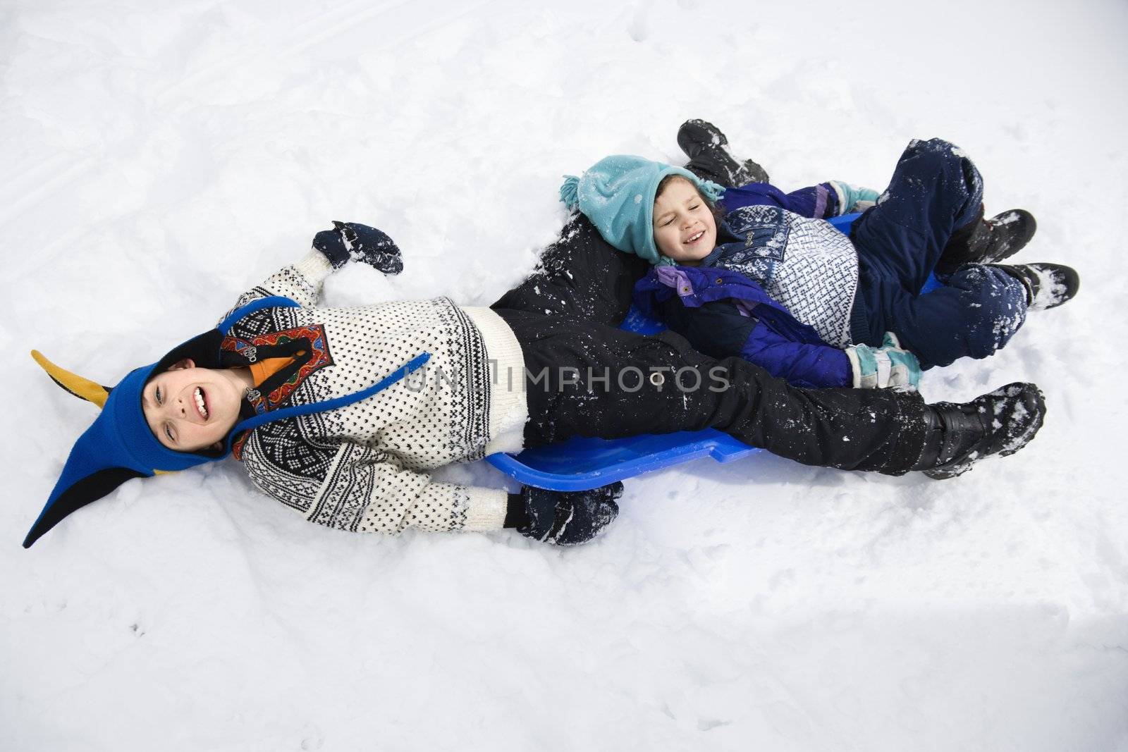 High angle view of Caucasian boy and girl lying on sled in snow.
