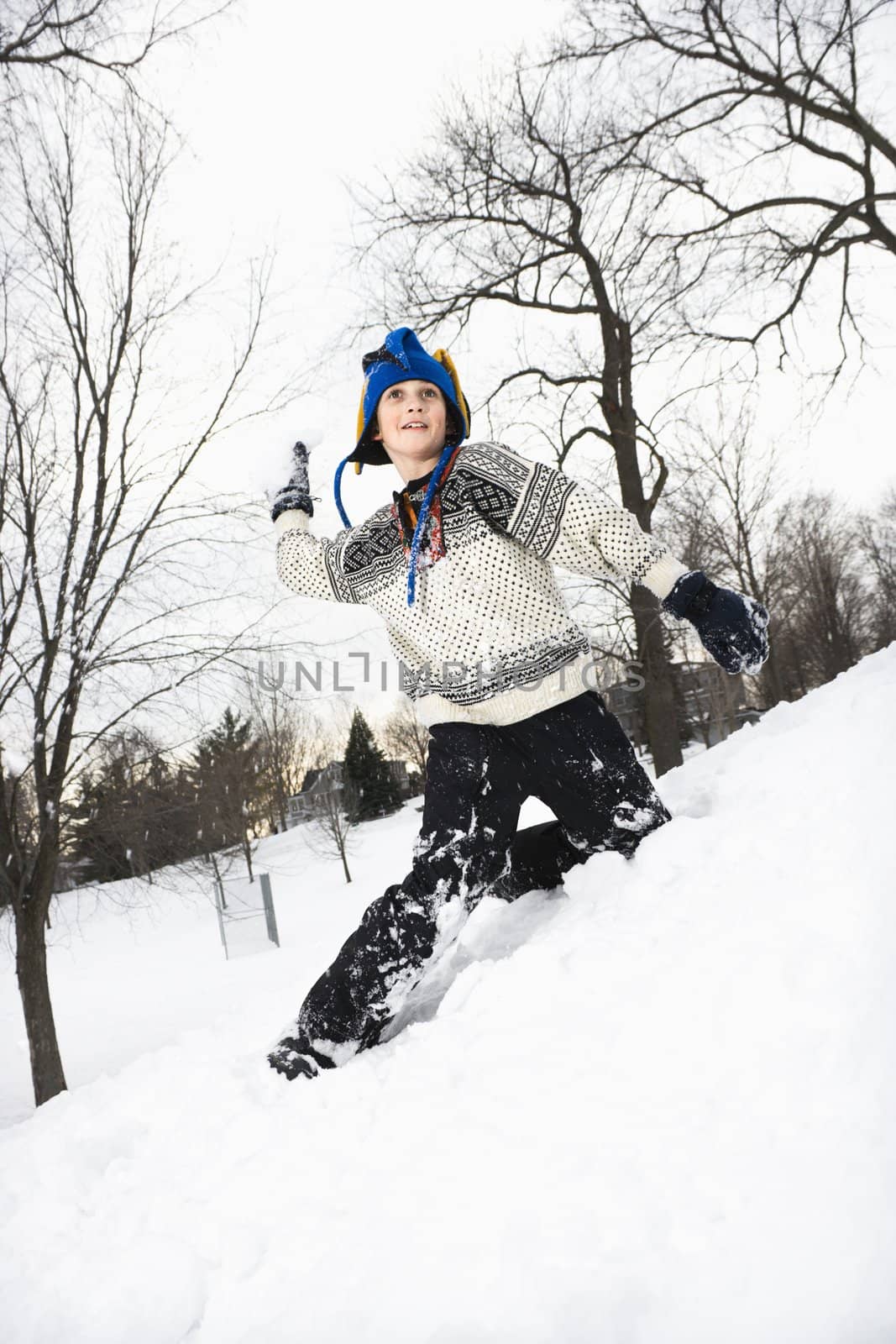 Caucasian boy wearing sweater and blue winter cap playing and throwing snow.