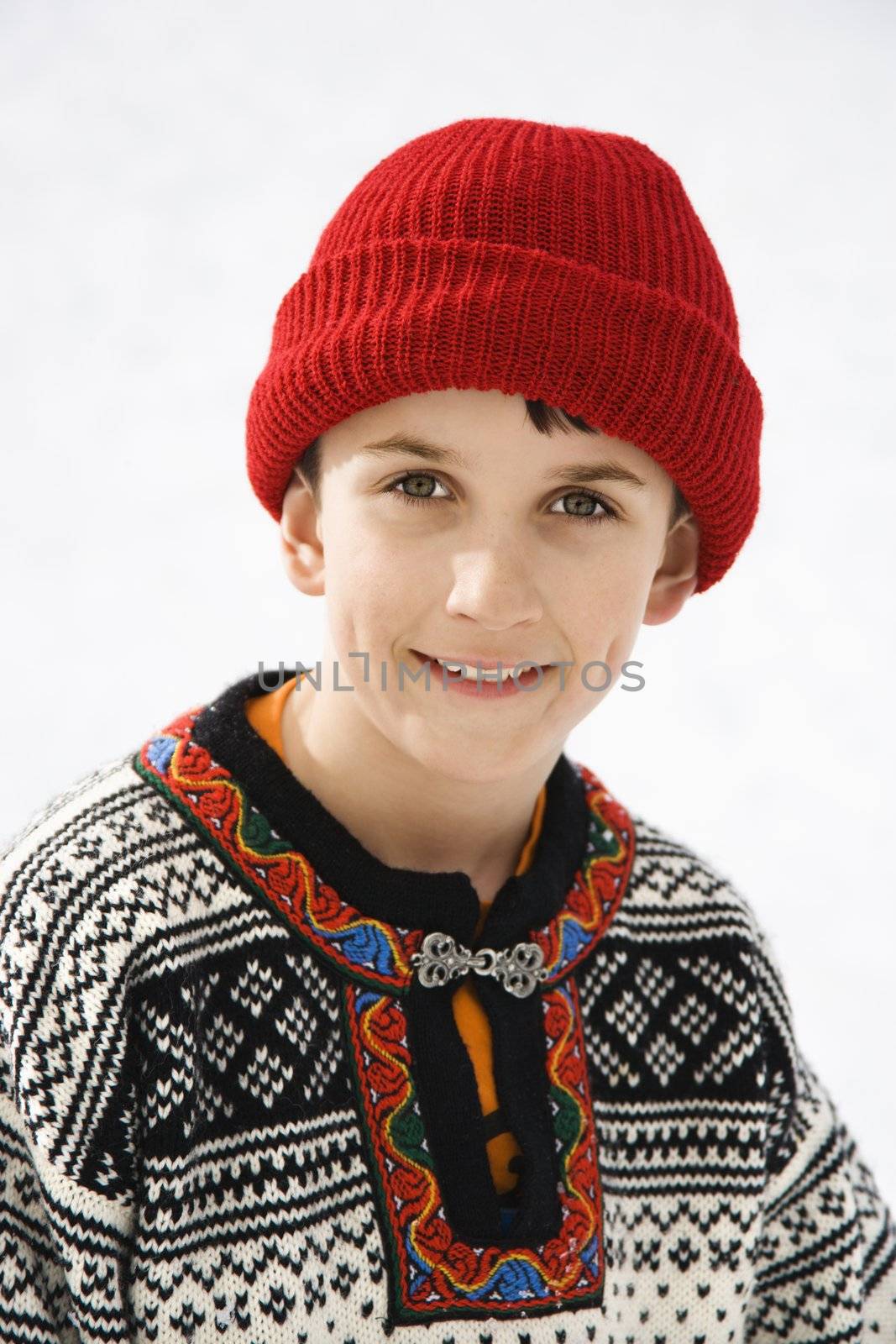 Portrait of Caucasian boy wearing sweater and red winter cap smiling at viewer.