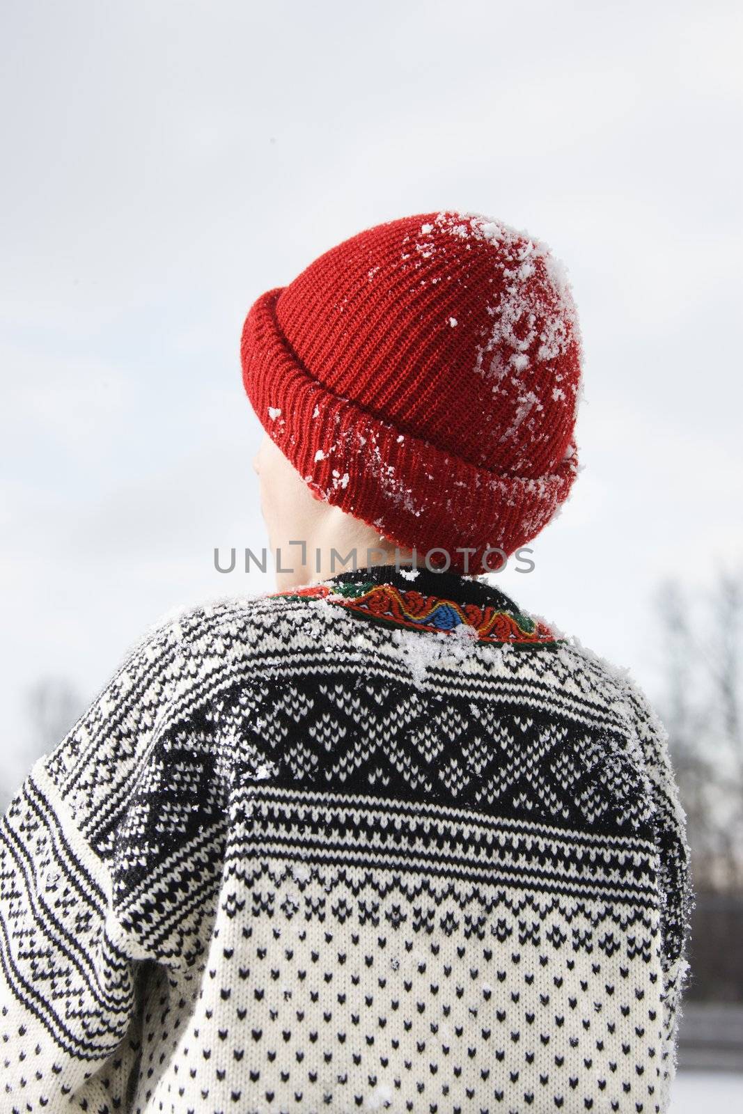 Back view of Caucasian boy wearing sweater and red winter cap.