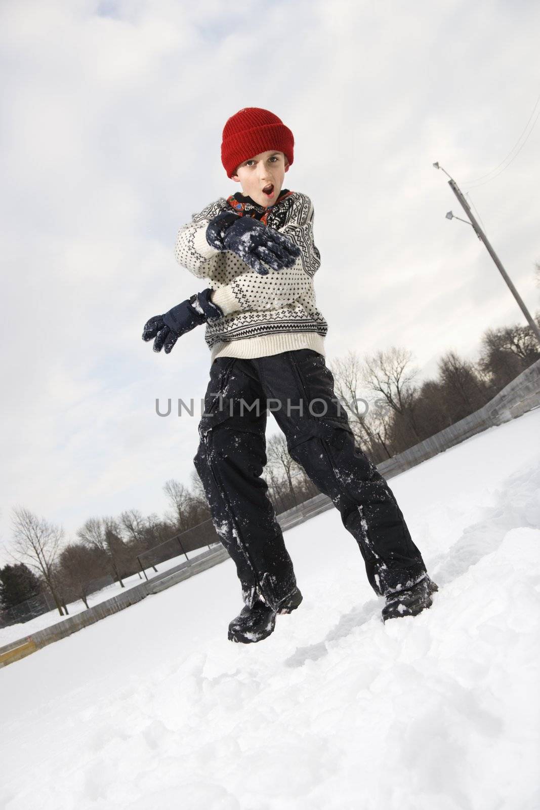 Caucasian boy with mouth open wearing sweater and red winter cap gesturing with arms and hands.