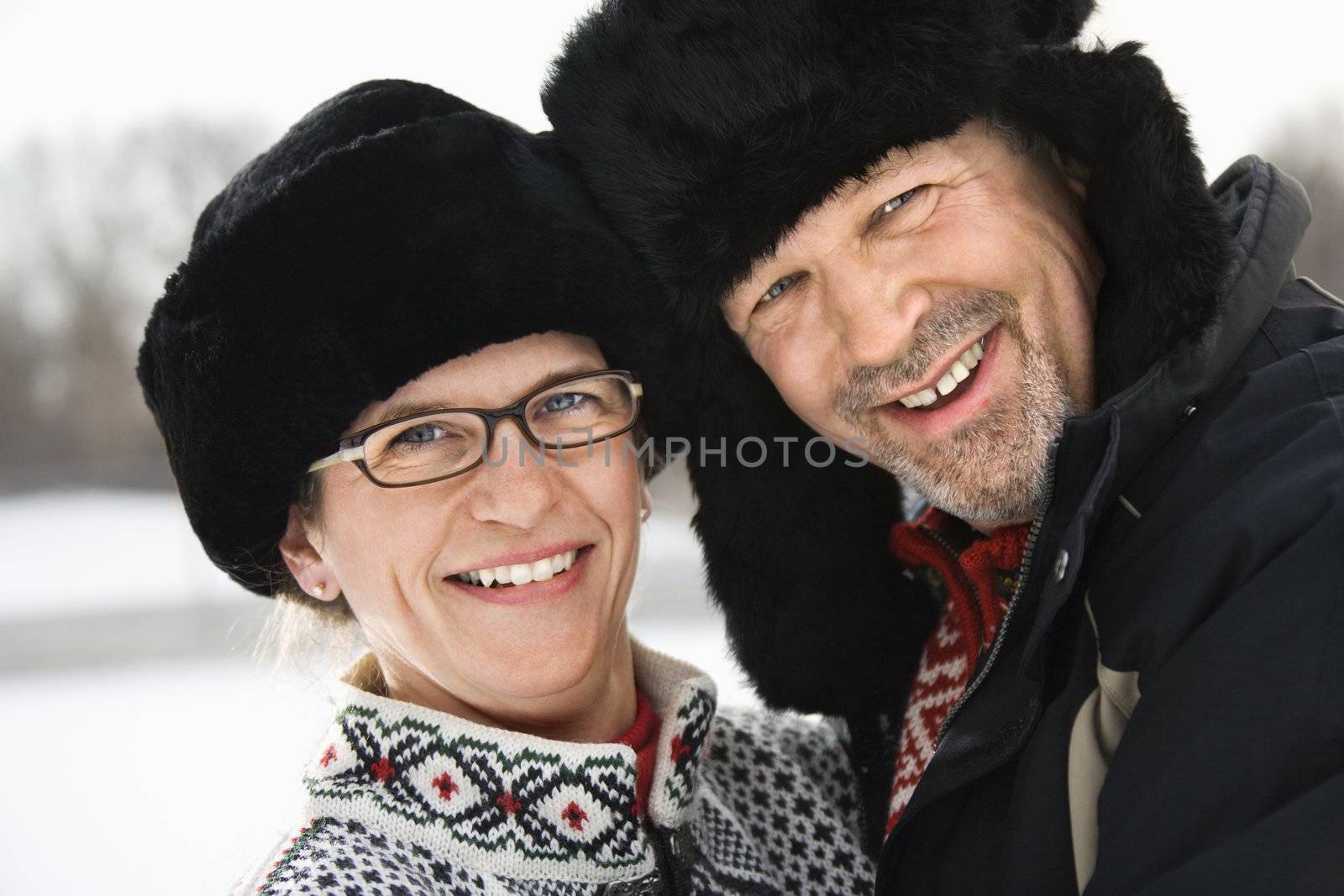 Portrait of happy Caucasian middle aged man and woman in winter clothing and black hats looking at viewer smiling.